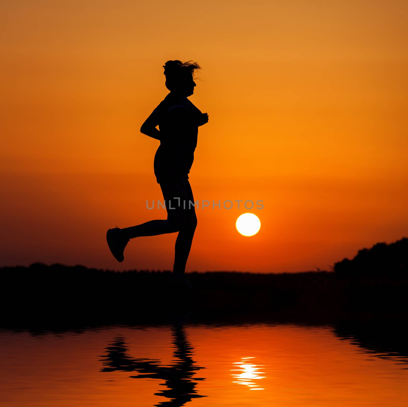 Silhouette woman running against orange sunset with reflection in water