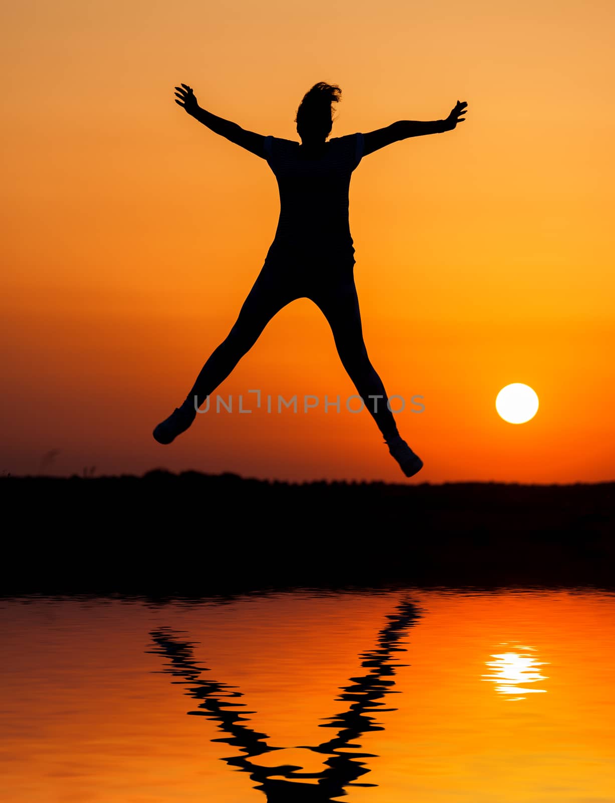 Silhouette woman jumping against orange sunset by Discovod