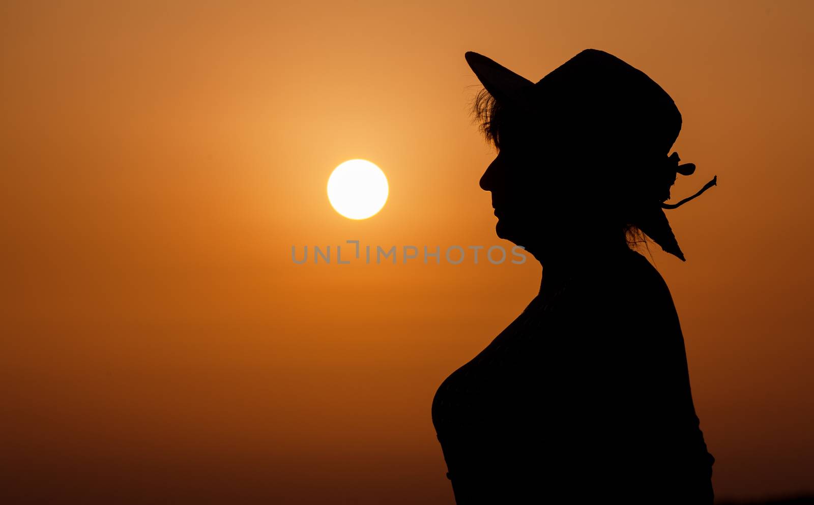 Silhouette woman portrait with hat against orange sunset