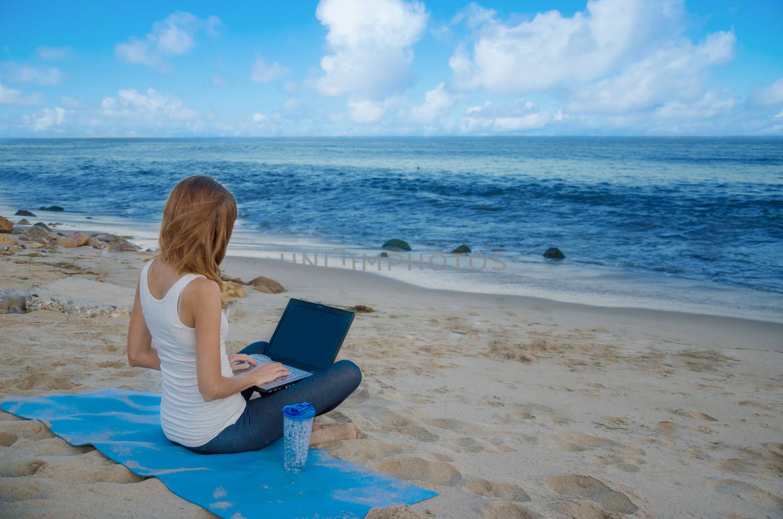 Young pretty woman with laptop on the beach by the ocean 