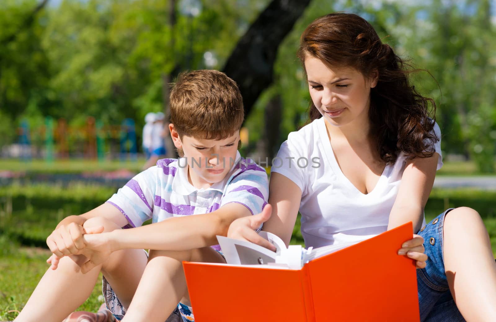 boy and a woman in a summer park reading a book together