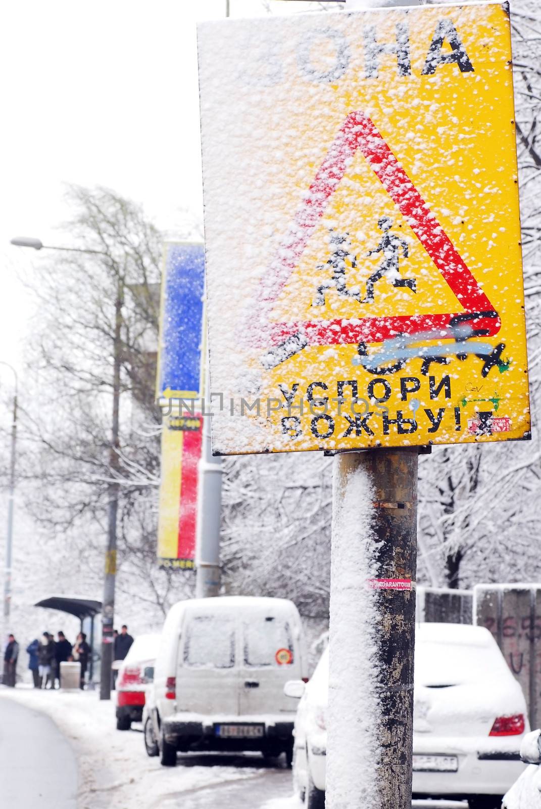 serbian traffic warning sign slow down, parked cars and bus station with people, at snow on street in Belgrade