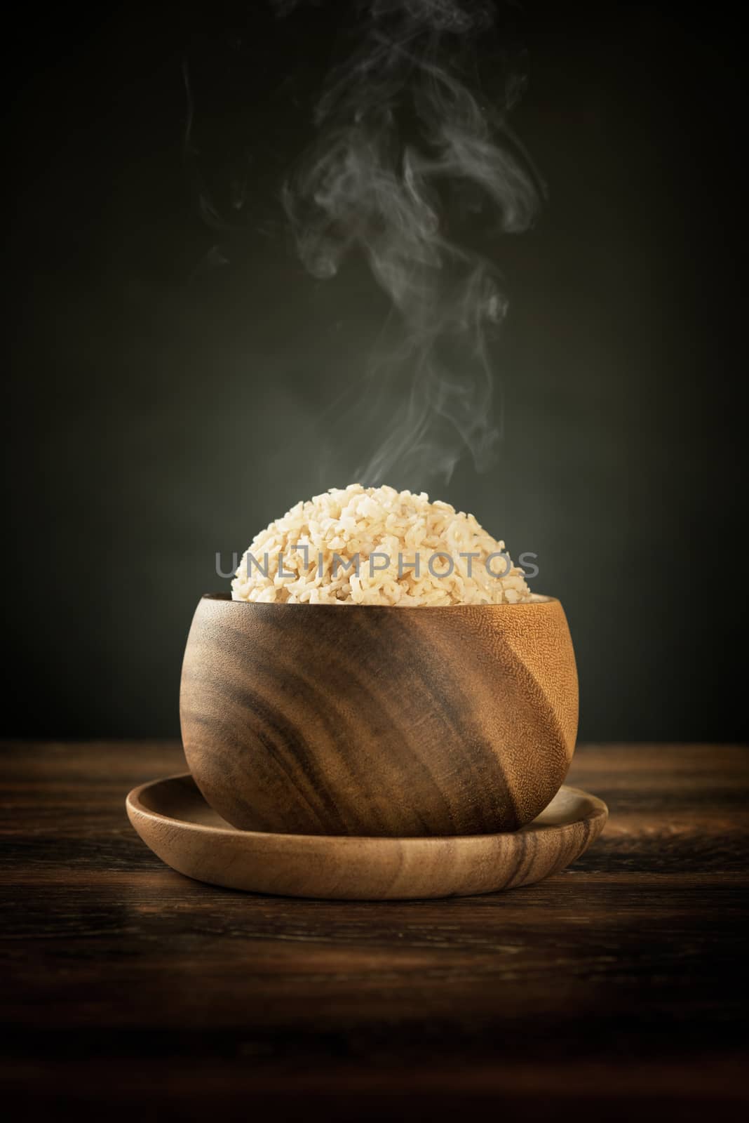 Cooked organic basmati brown rice in wooden bowl with hot steam smoke on dining table. Low light setting.