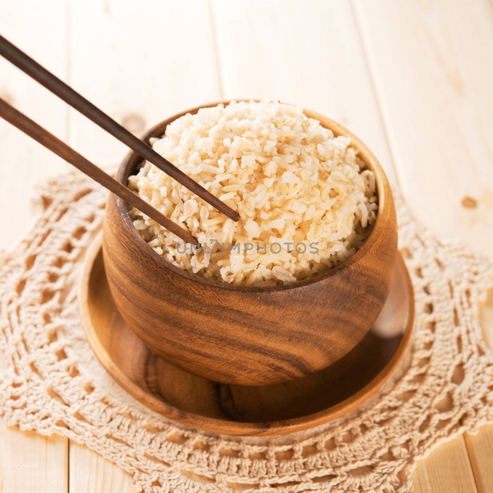 Close up cooked organic basmati brown rice in wooden bowl with chopsticks on dining table.