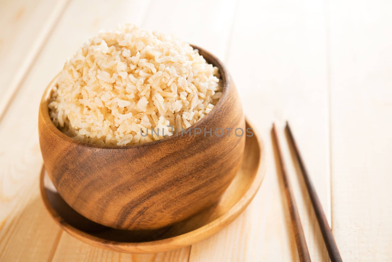 Cooked organic basmati brown rice in wooden bowl with chopsticks on dining table.