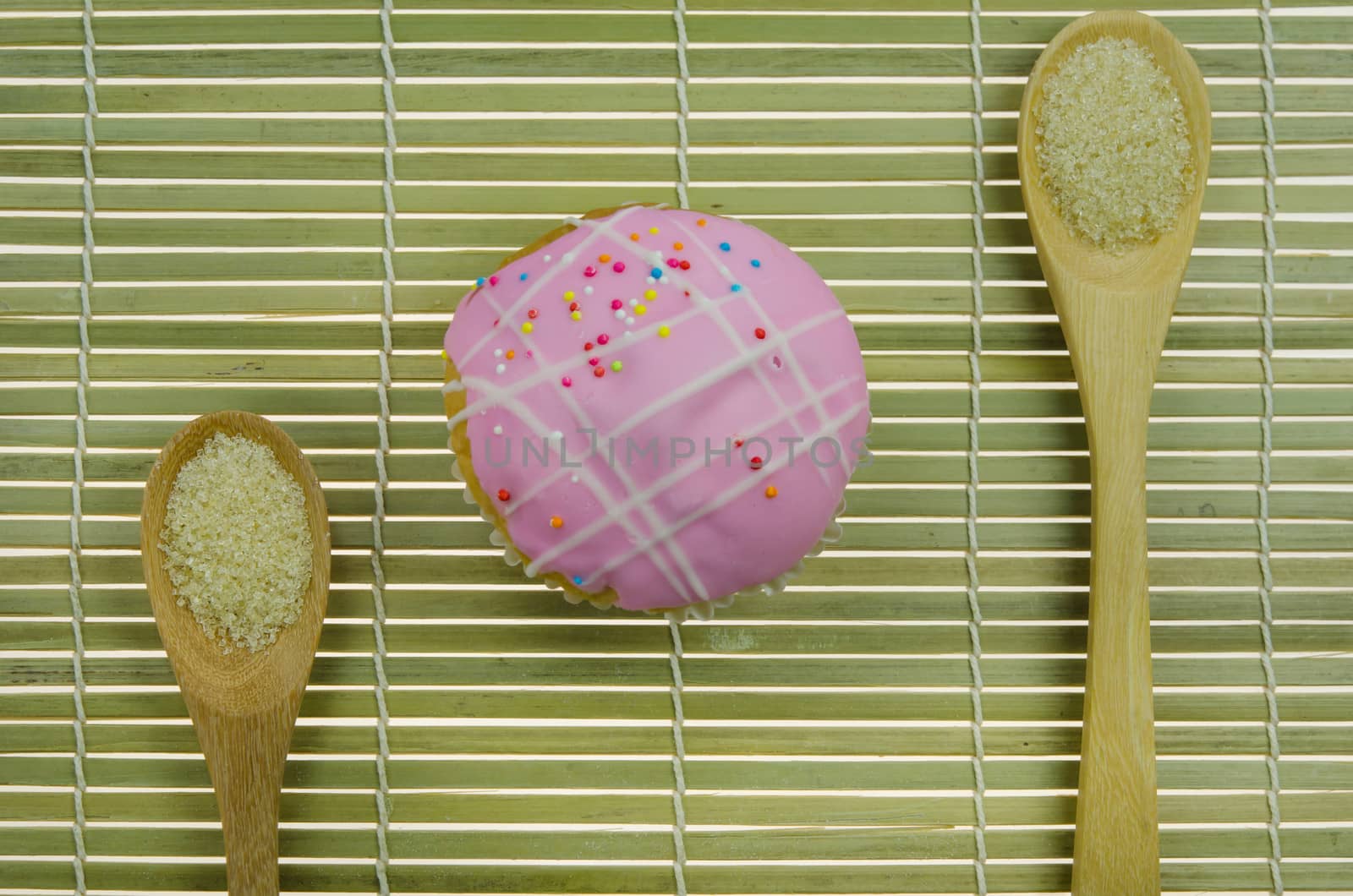 top view pink cupcake with colorful sprinkles and spoon of sugar on wooden background