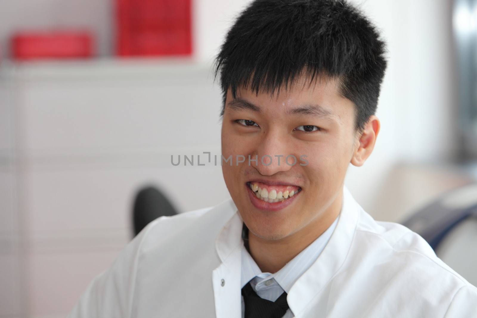 Head and shoulders portrait of a smiling young male Asian technician in a white lab coat