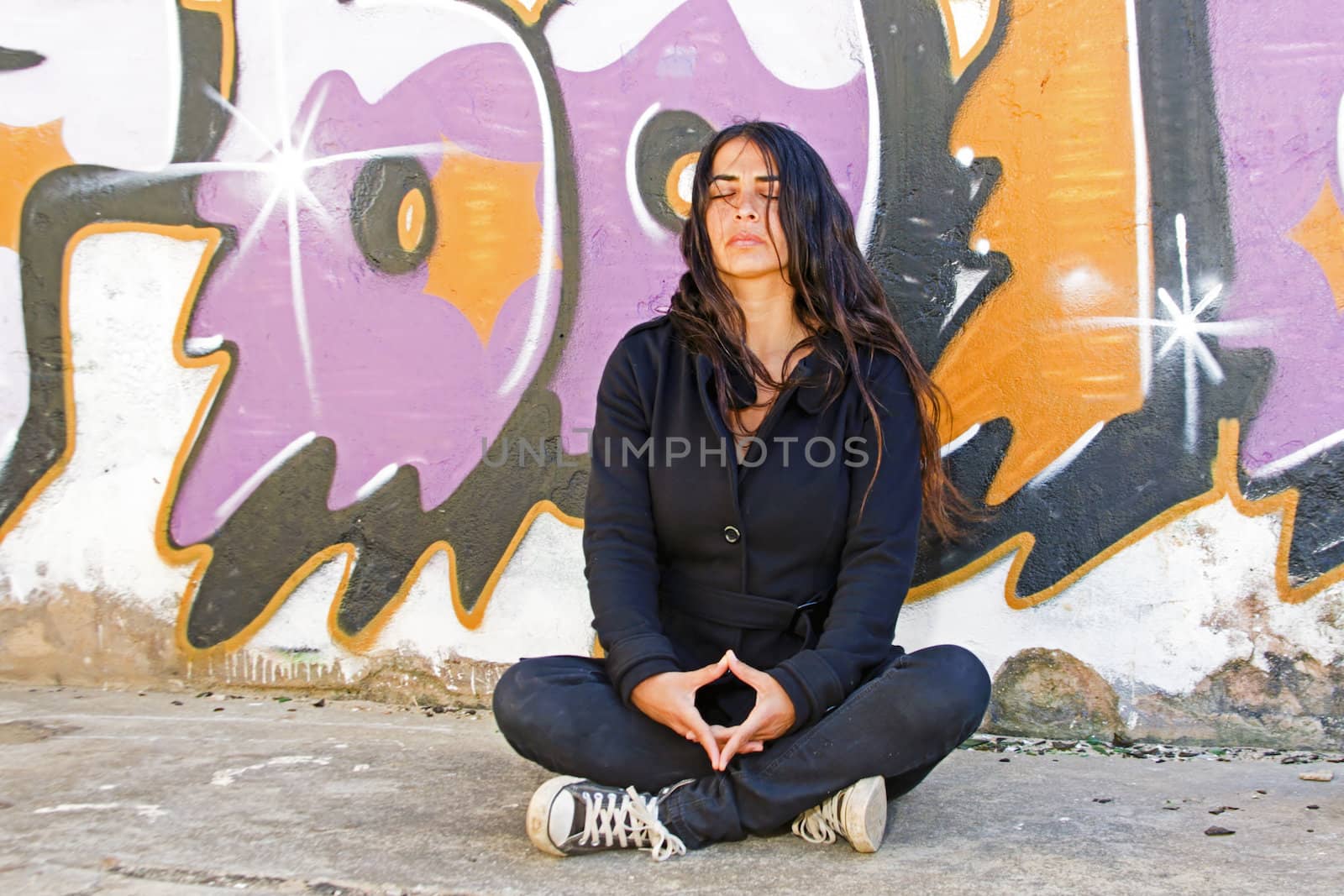 Young woman meditating at a graffiti brick wall by devy