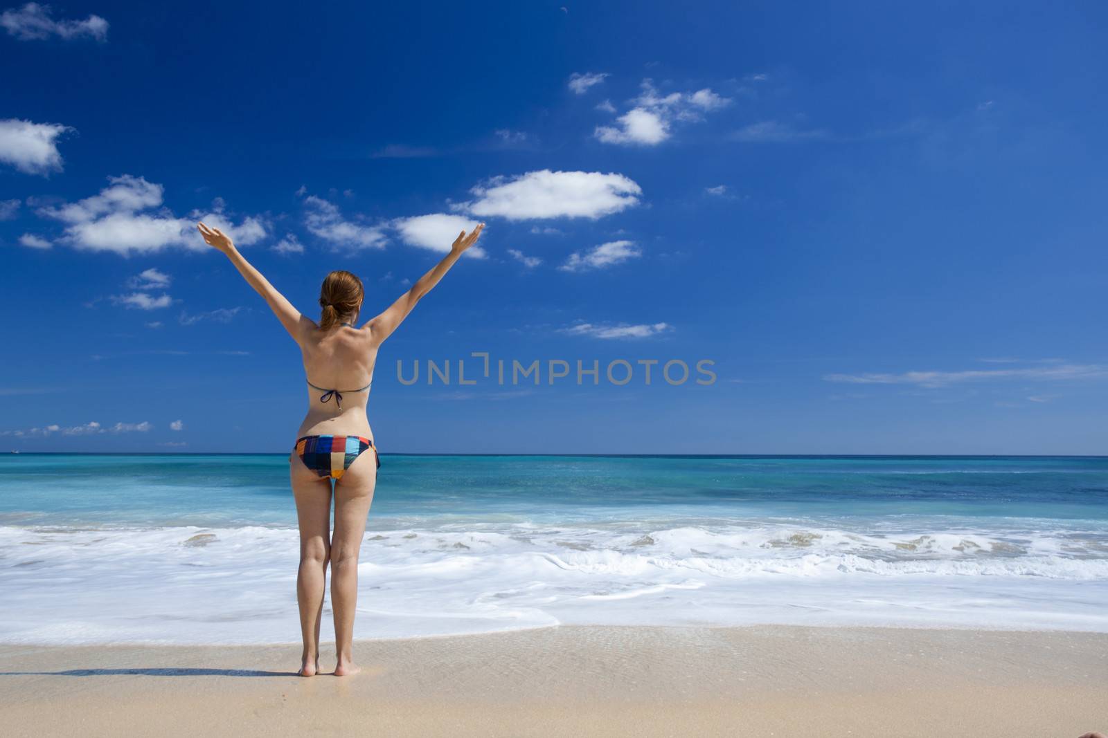 Beautiful young woman with arms open in a tropical beach enjoying the summer 