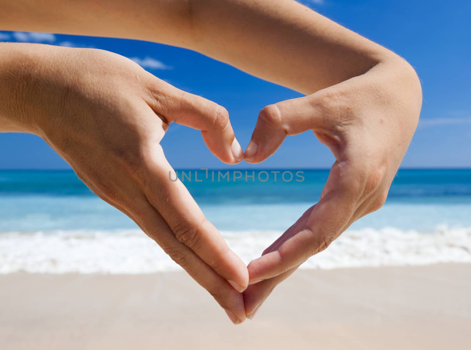 Female hand making a heart shape against a beautiful blue sky