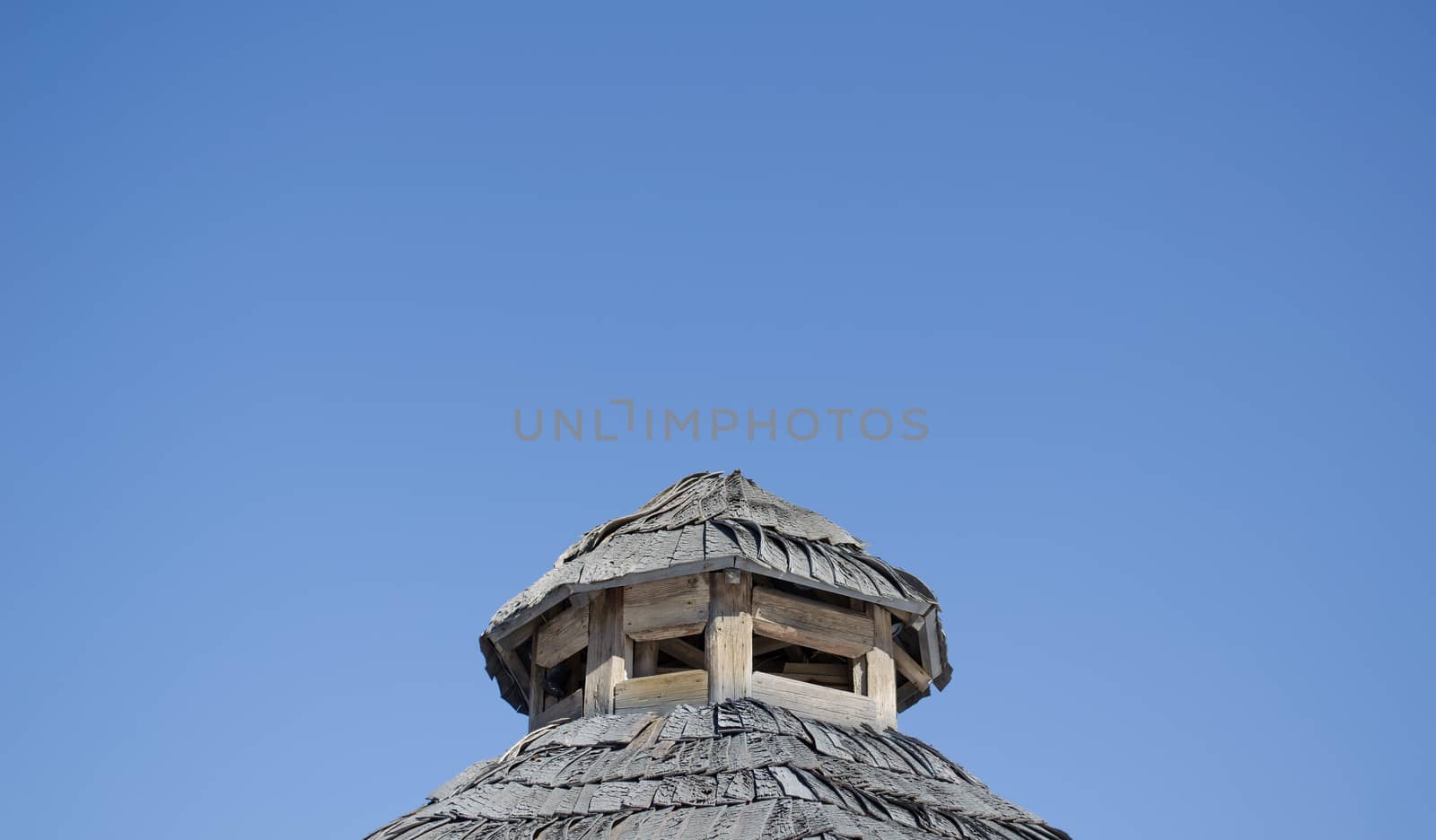 vintage old rural house roof coated with wooden tiles on background of blue sky.