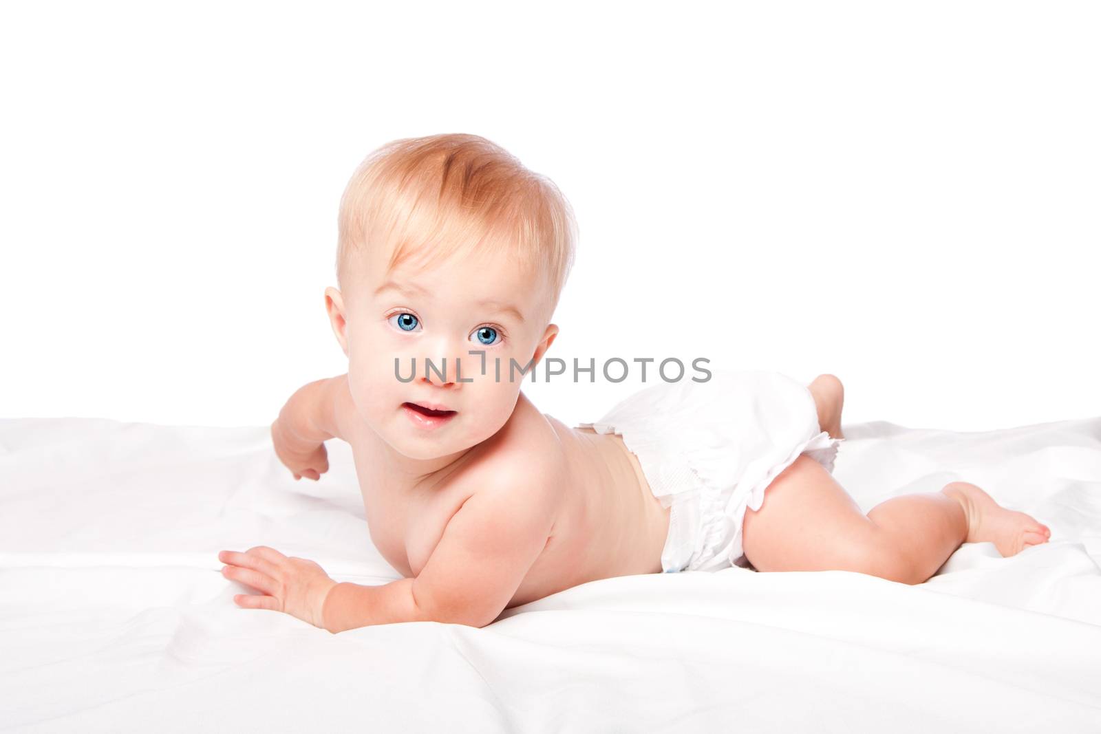 Cute happy infant baby with blue eyes wearing diapers laying on belly, on white.