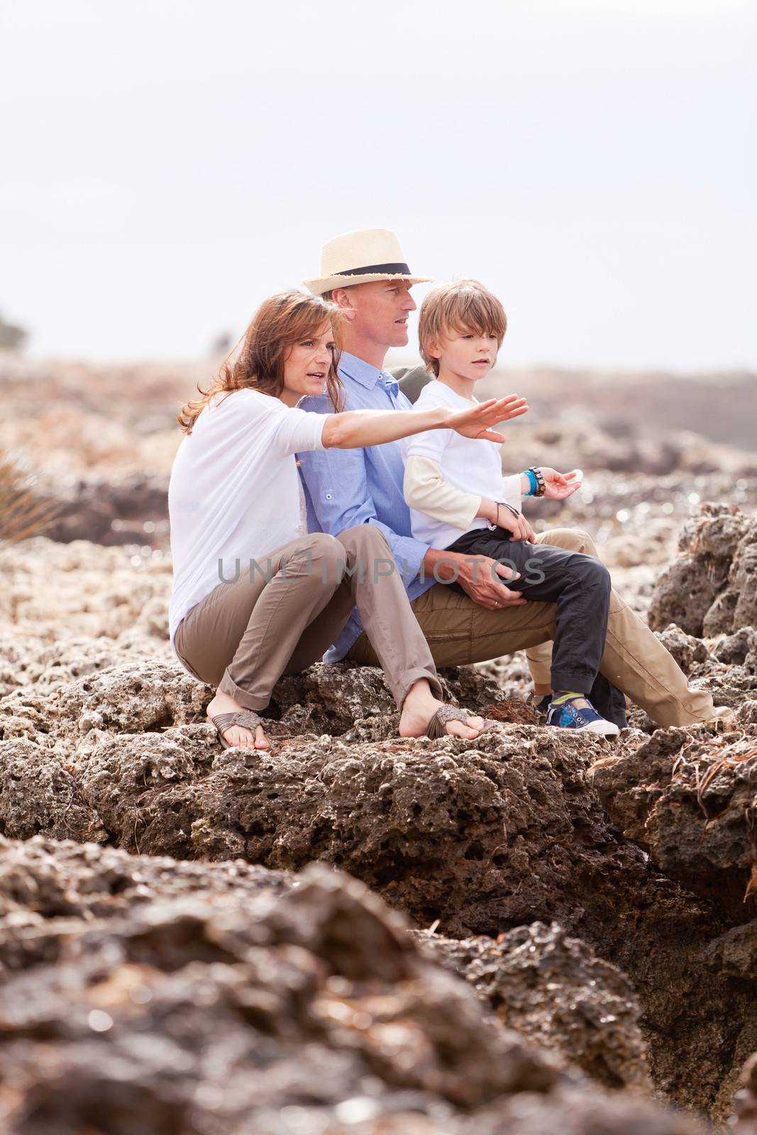 happy family sitting on rock and watching the ocean waves by juniart