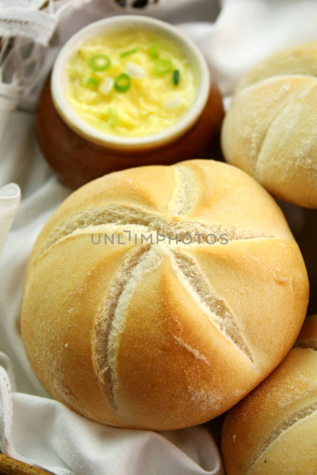 Fresh round breadrolls with a jar of butter and diced spring onions.