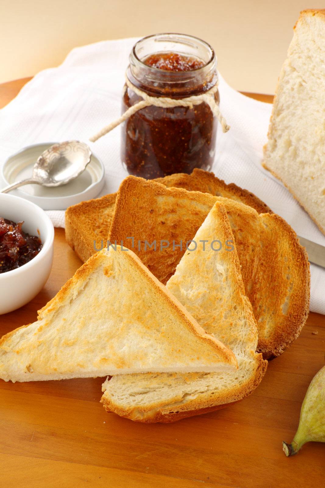 Jar of homemade fig jam with a toast slices of crusty bread.