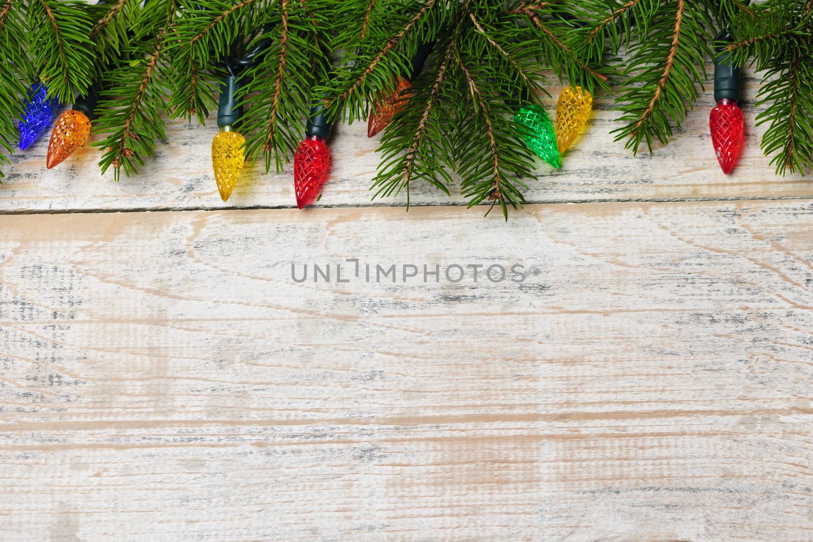 Multicolored Christmas lights on spruce branch with wooden background
