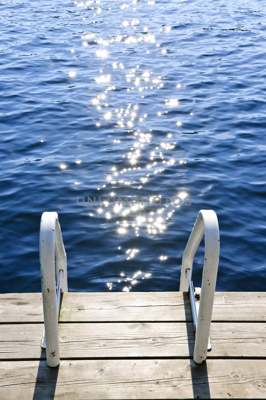 Dock on summer lake with sparkling water by elenathewise