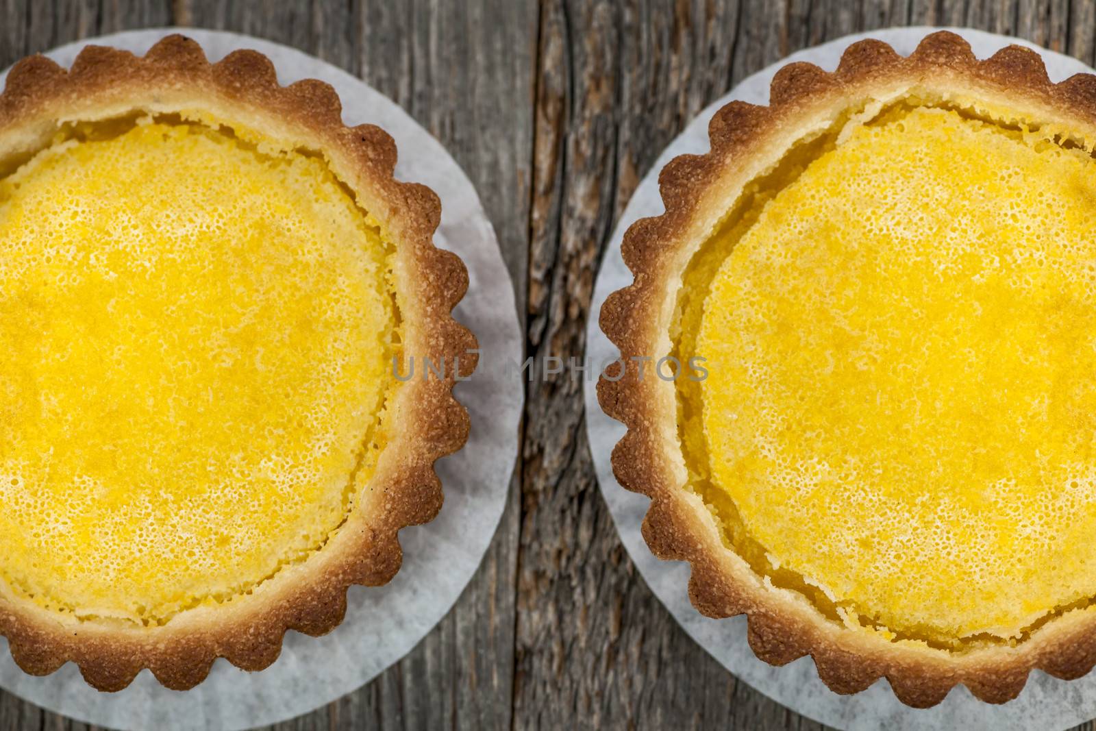 Two fresh gourmet lemon dessert tarts on wood background from above