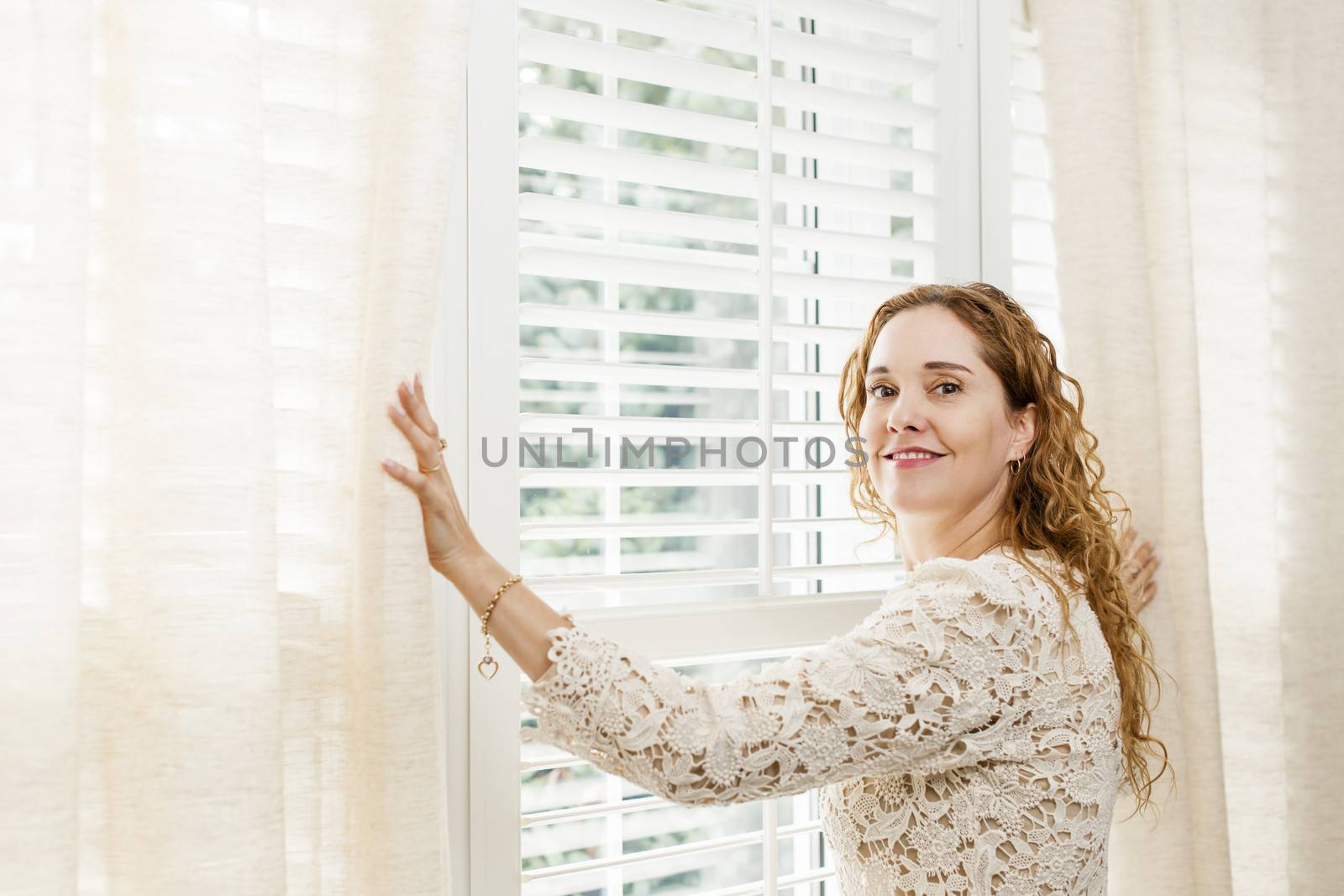 Happy woman opening curtains on big sunny window with shutters