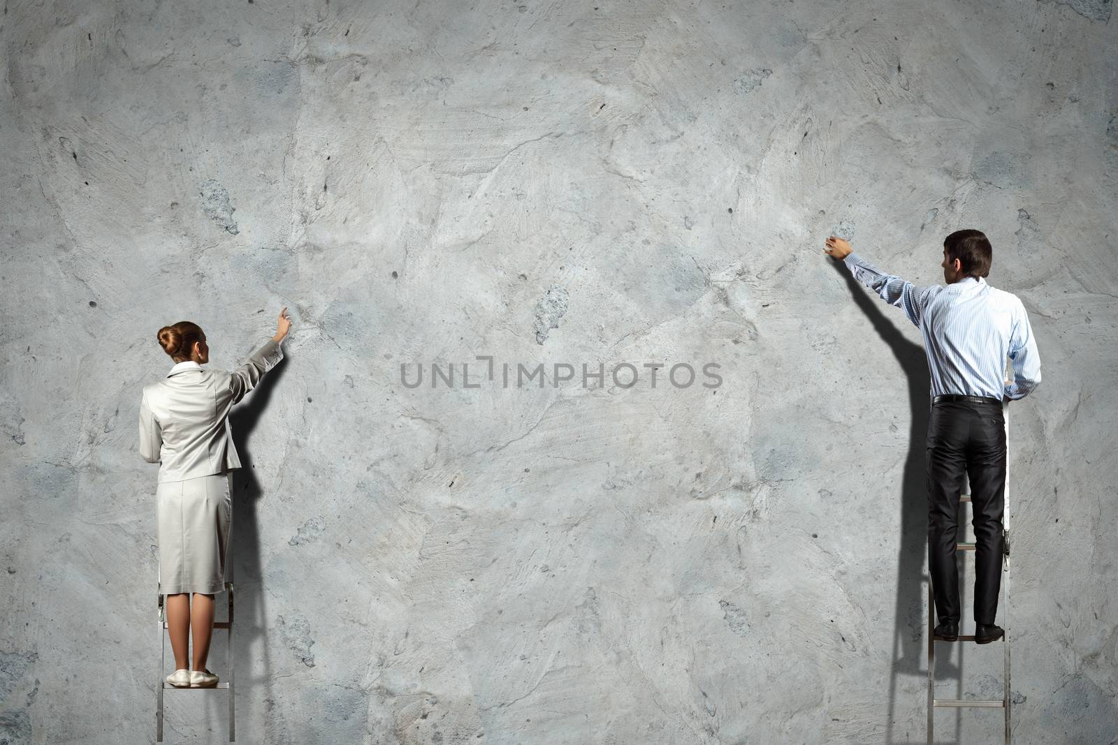 businesspeople standing on ladder drawing diagrams and graphs on wall