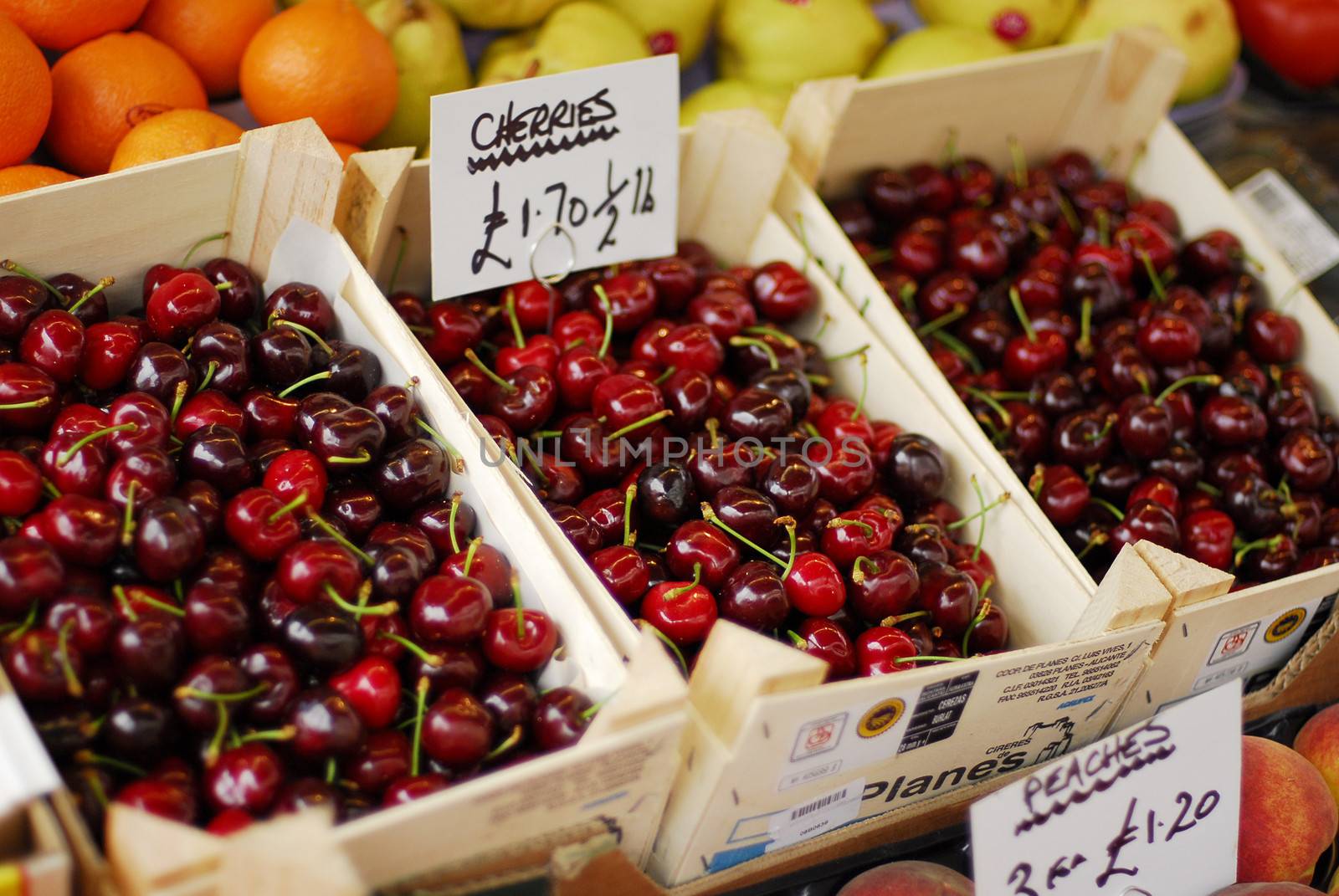 Cherries in focus along with other fruits being sold at market
