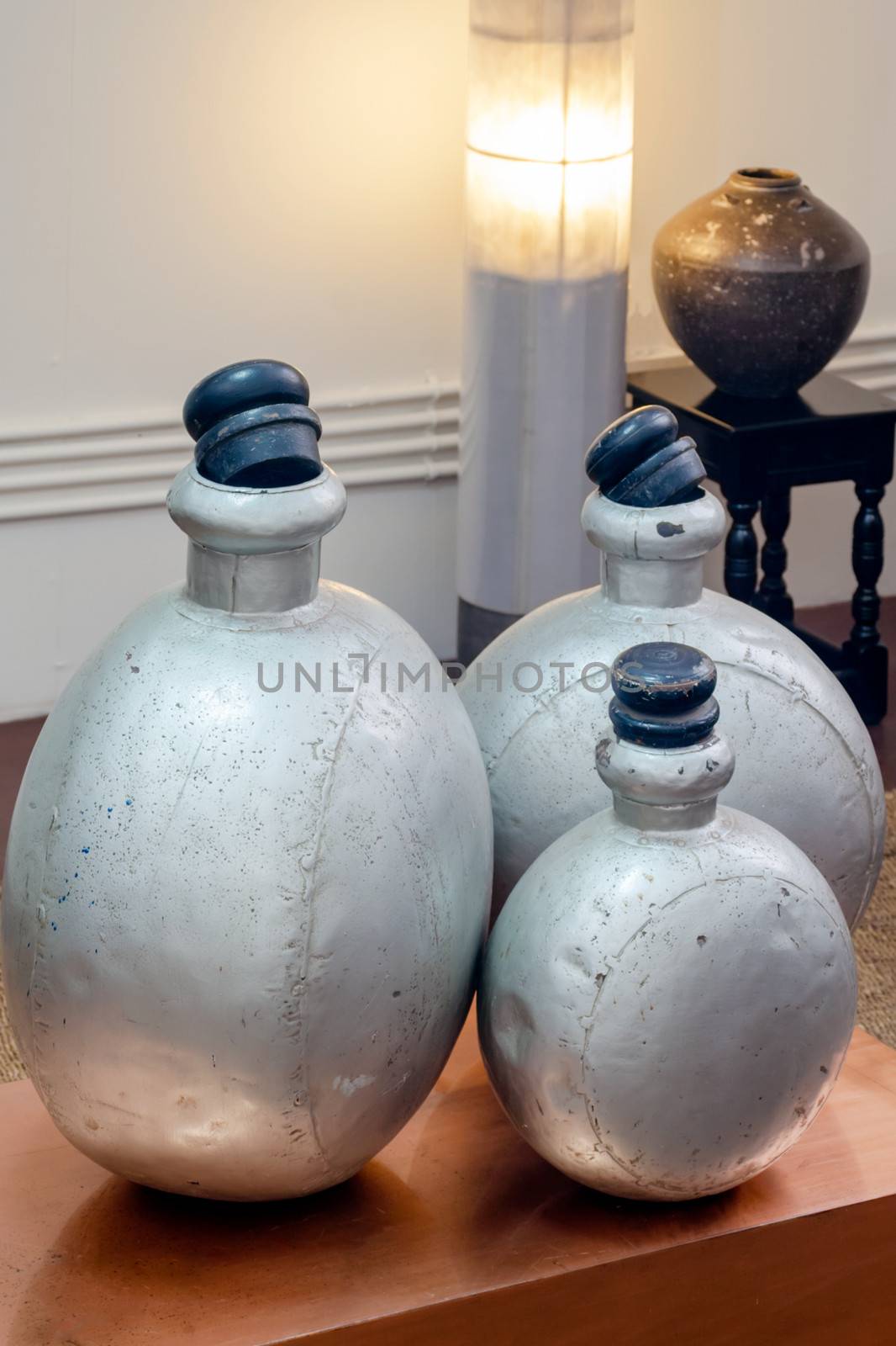 Vertical color portrait in a studio showroom interior displaying old industrial aluminium chemical bottles standing on a copper plated occasional table. Other features and props include pottery stand table standard lamp, generic  shot location was Bombay India, available with property release.