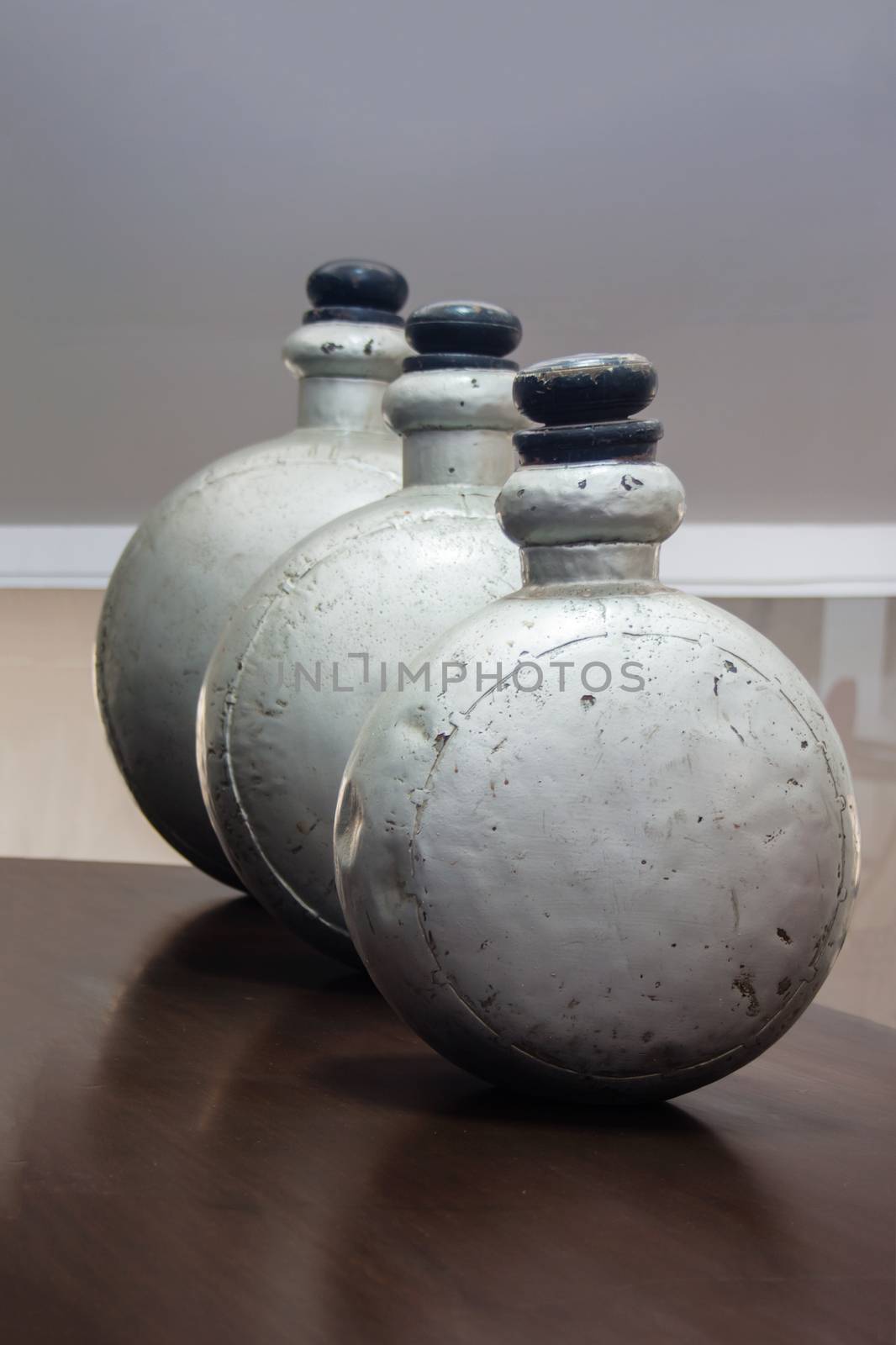 Vertical color portrait in a studio showroom interior displaying old industrial aluminum chemical bottles standing on a laminated dark wood table. Location for this  generic shot was Bombay India, available with property release.