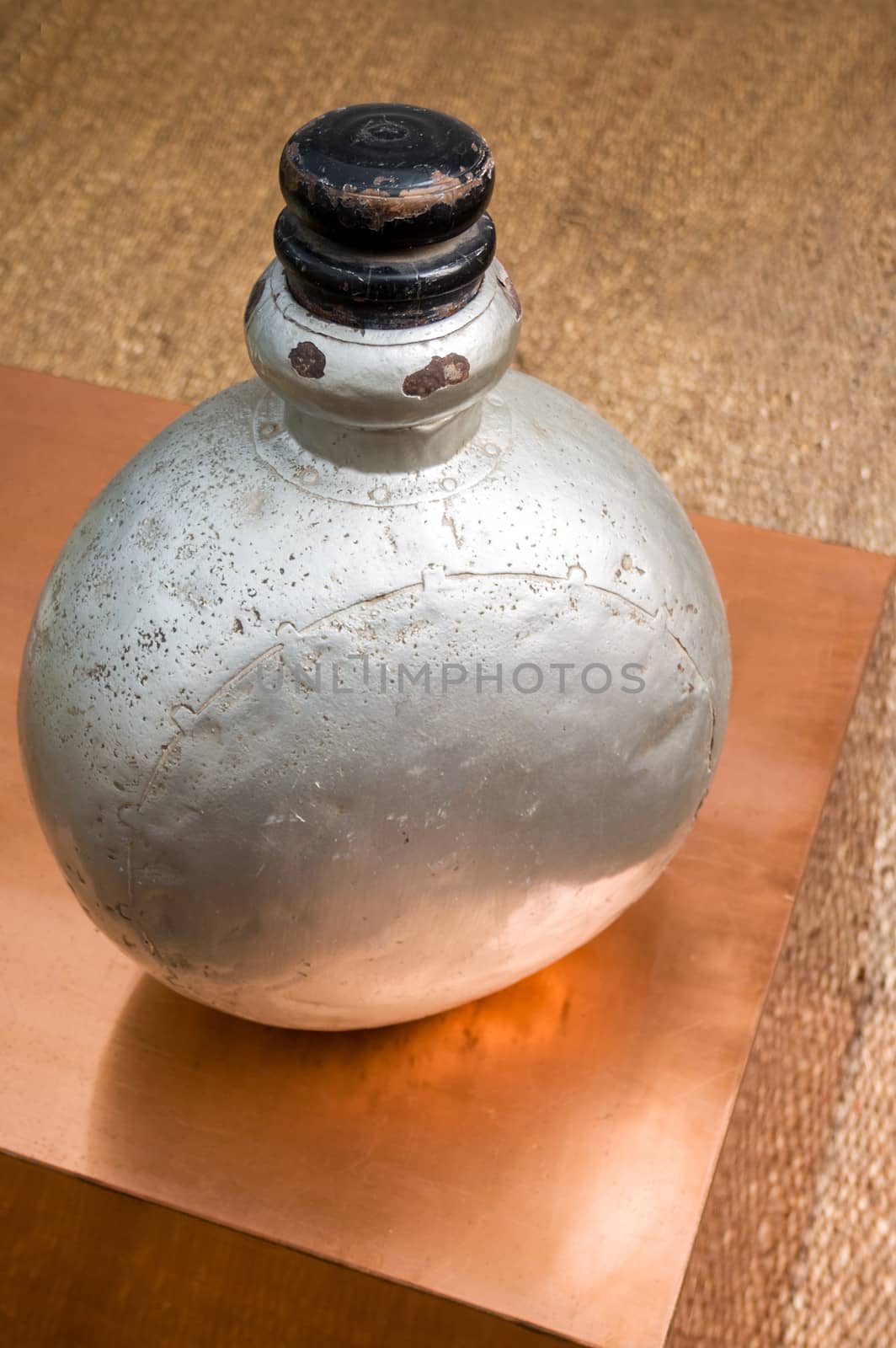 Vertical color portrait in a studio showroom interior displaying old industrial aluminum chemical bottle standing on a copper plated occasional table. Generic shot location was Bombay India, available with property release.