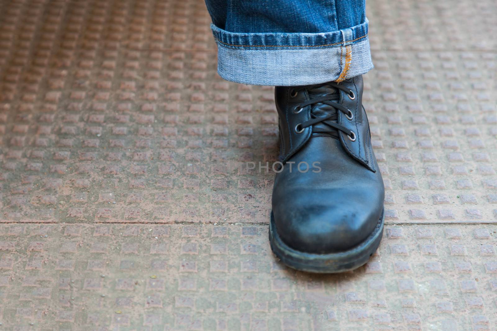 Horizontal color landscape of trendy laced up leather boots and stylish turned up denim jeans on a stippled tiled ground. Generic shot of global appeal shot in Bombay India