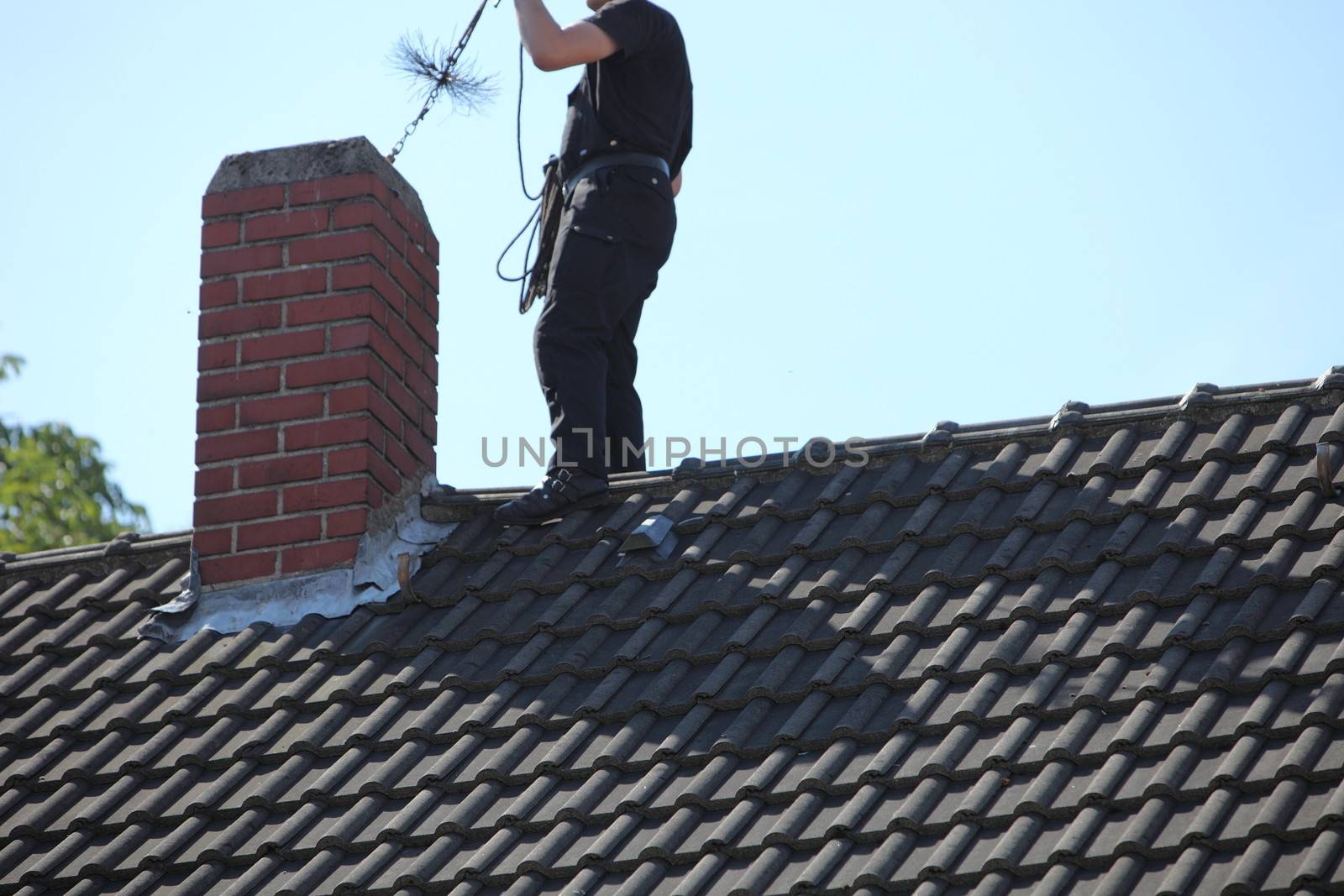 Chimney sweep at work on the roof of a house busy inserting a chain and wire brush into the flue from above