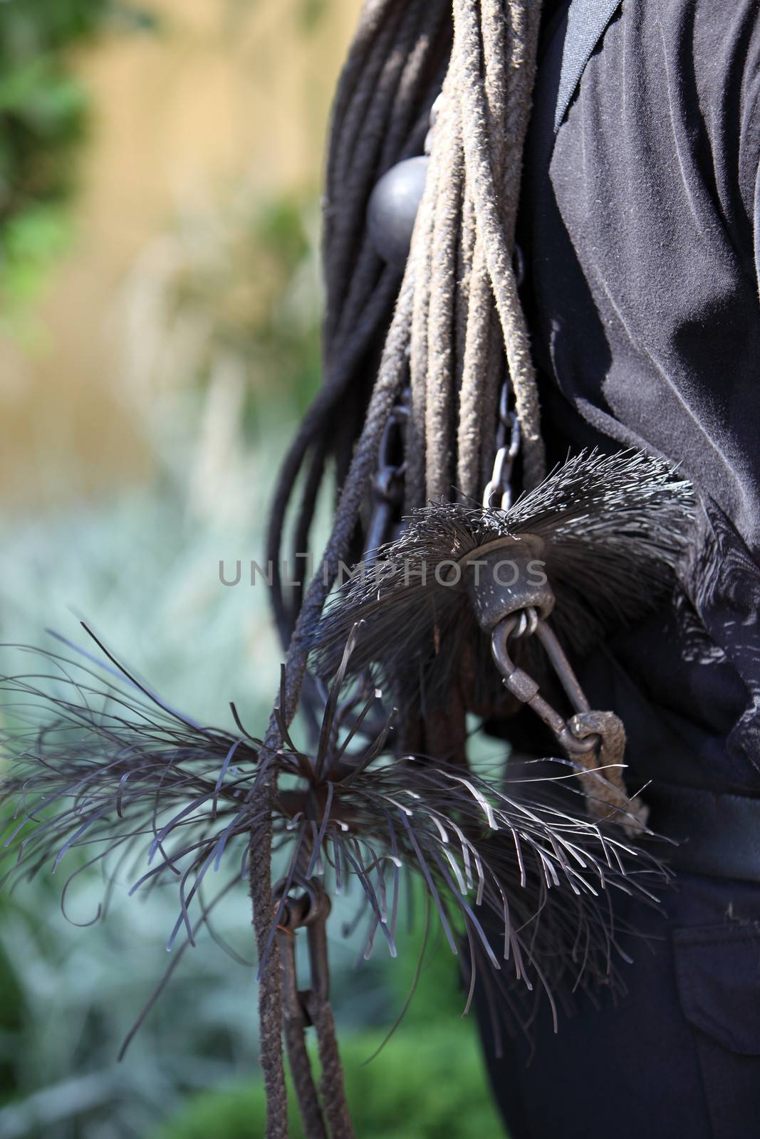 Coarse wire brushes and euipment of a chimney sweep slung over the back of a workman, close up view