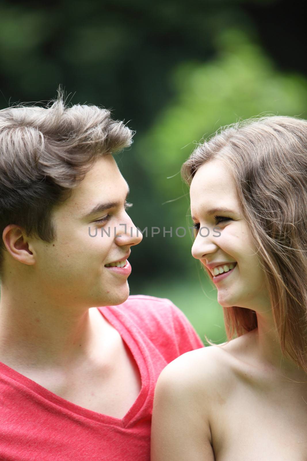 Attractive romantic young teenage couple laughing and smiling adoringly into each others eyes , closeup portrait
