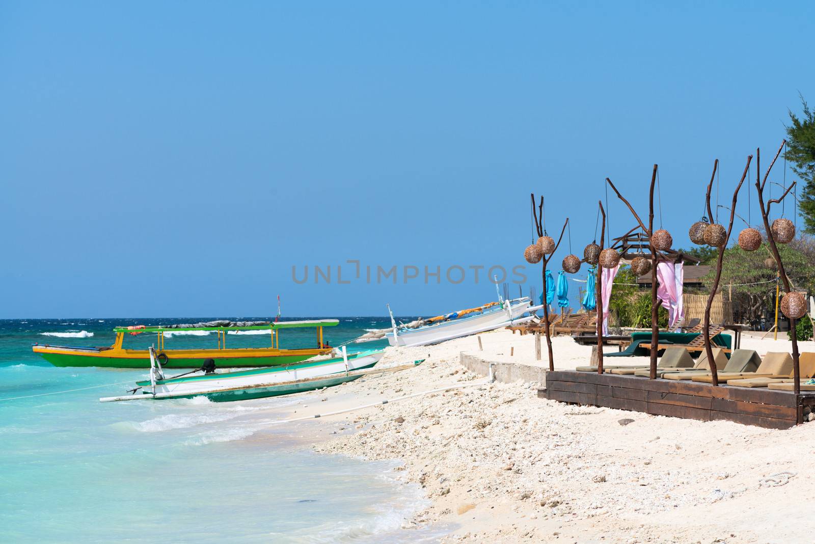 Small wooden tourist and fishing long boats near sand beach with cafe and beach beds in front, Gili Trawangan island, Indonesia 