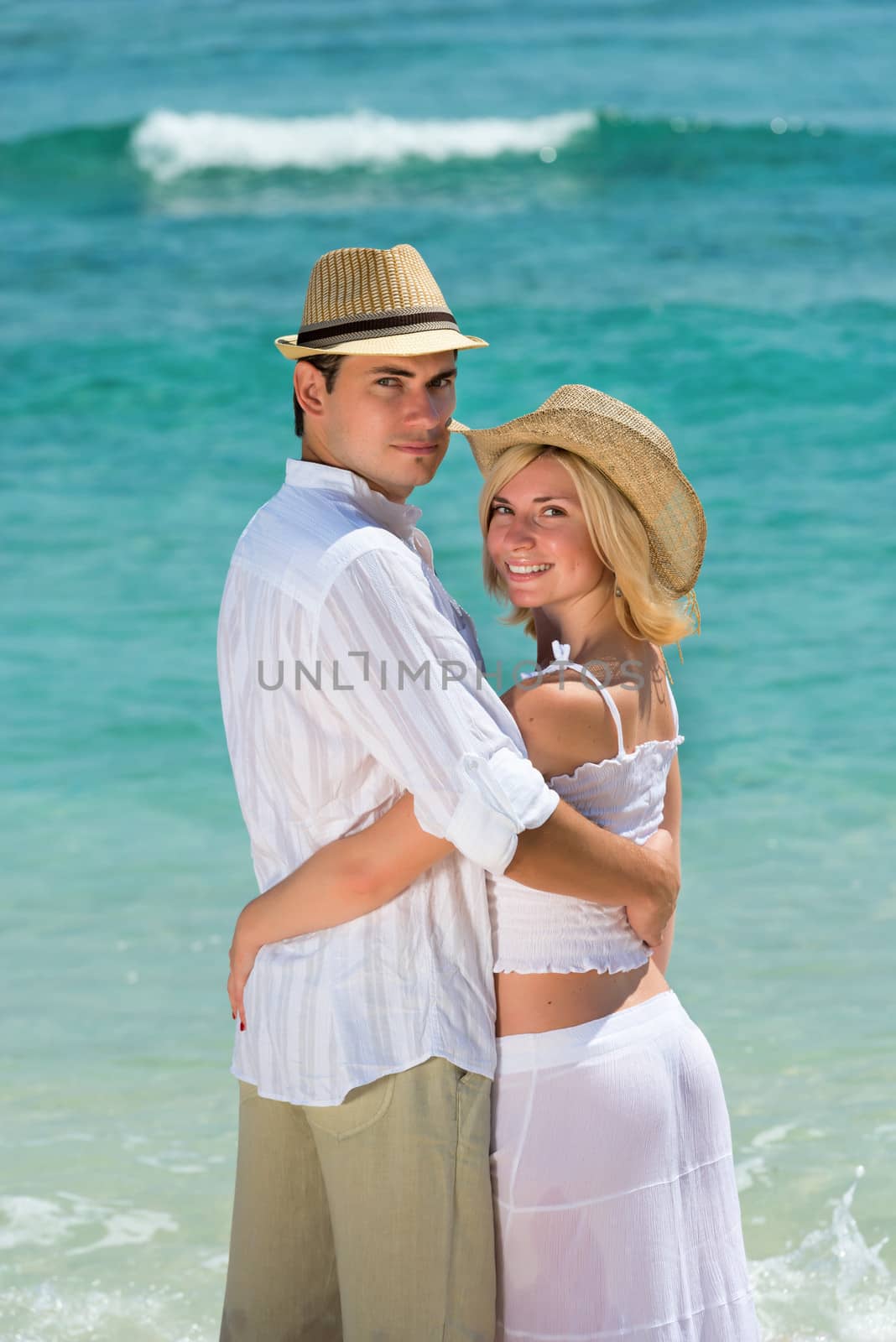 Happy young couple in hats enjoying at beach with blue sea on background