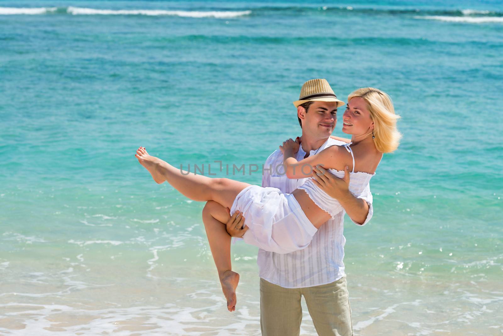 Happy young man carry woman. Couple enjoying at beach with blue sea on background.