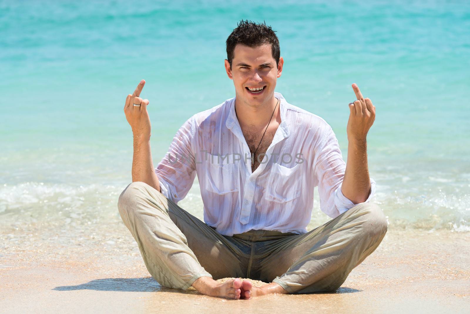 Happy man showing middle finger and enjoying at beach with blue sea on background