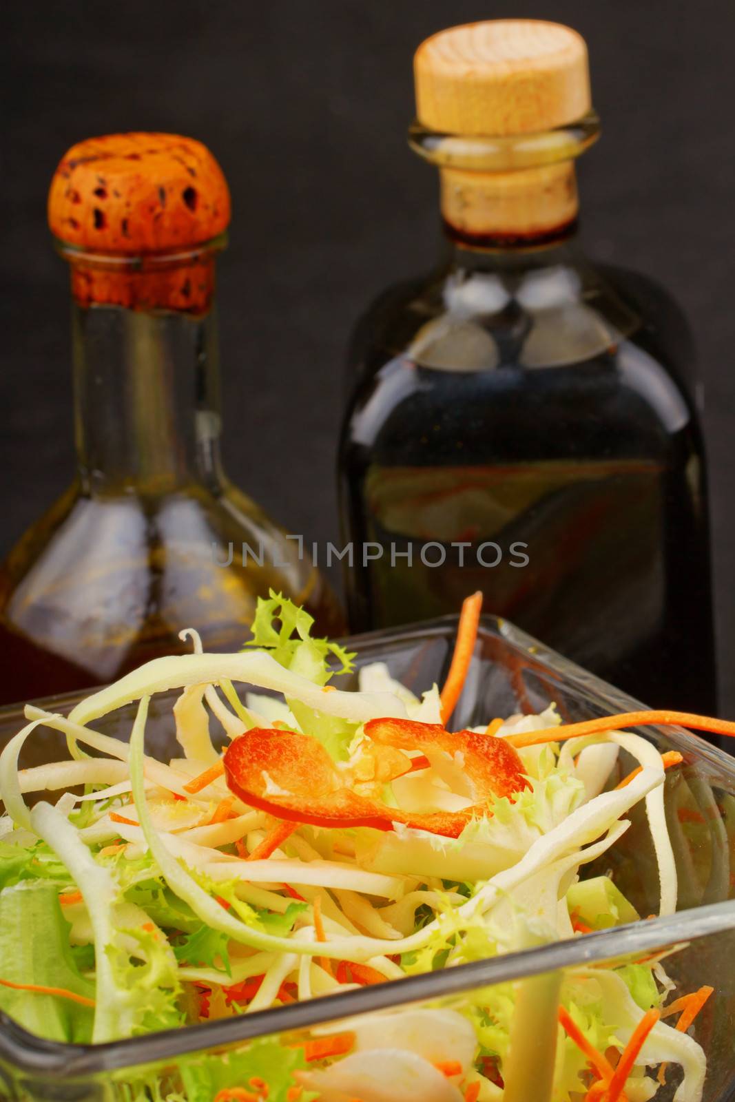 Close up of glass cup with salad, with vinegar and oil on the back