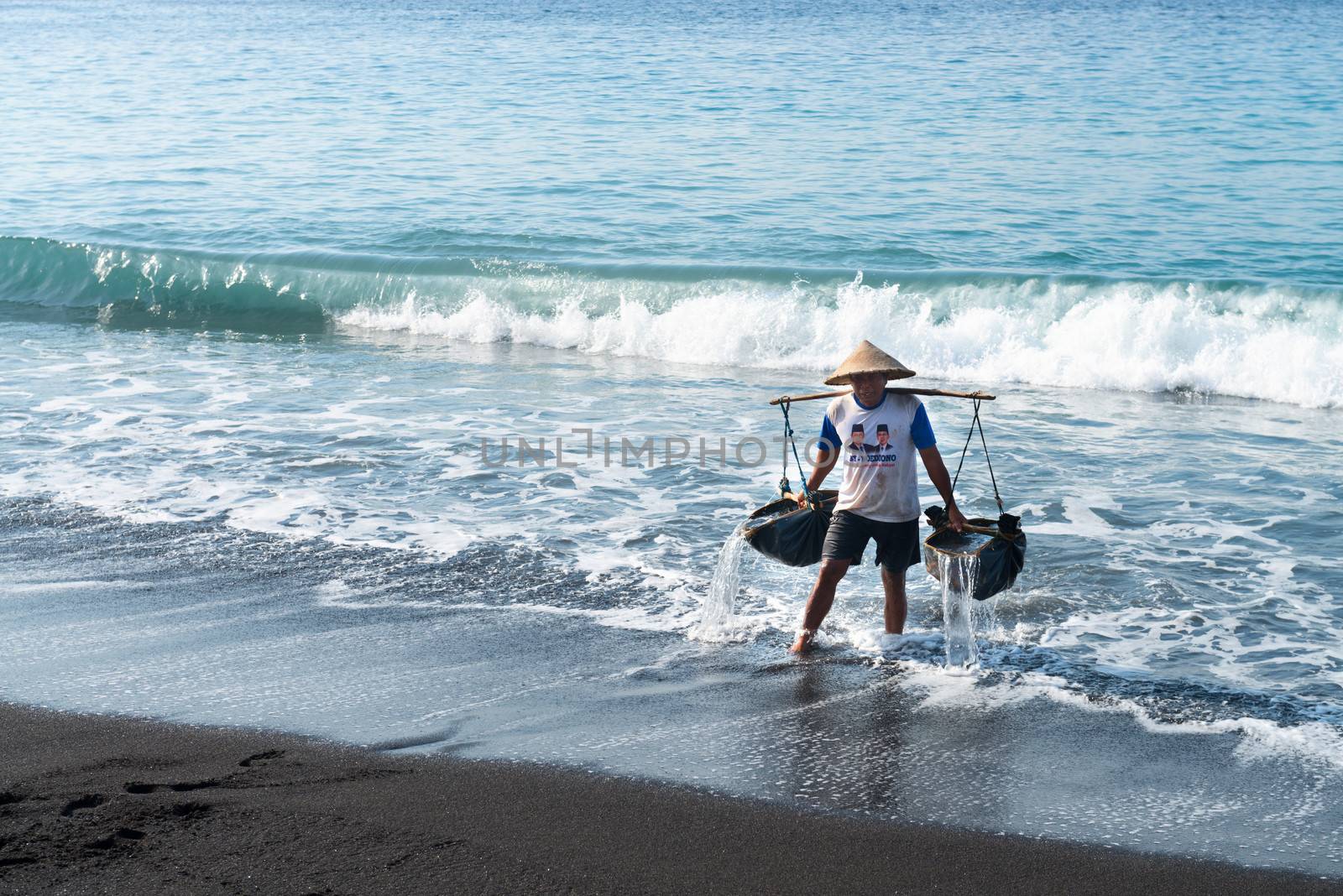 BALI - SEP 26: Manual male worker collects water for sea salt production on Sep 26, 2012 in Amuk Bay, Bali. It is unique tradition of salt production on volcanic sand dating back over 900 years. 