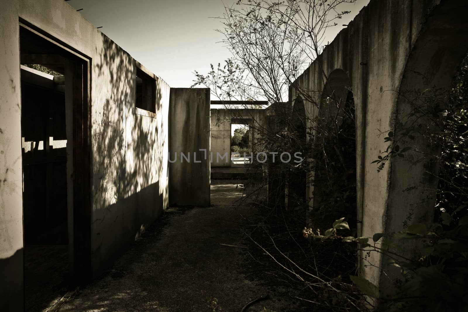 Dark gloomy image of a dilapidated abandoned building without a roof and a view right through the building out of an old doorway to the countryside beyond