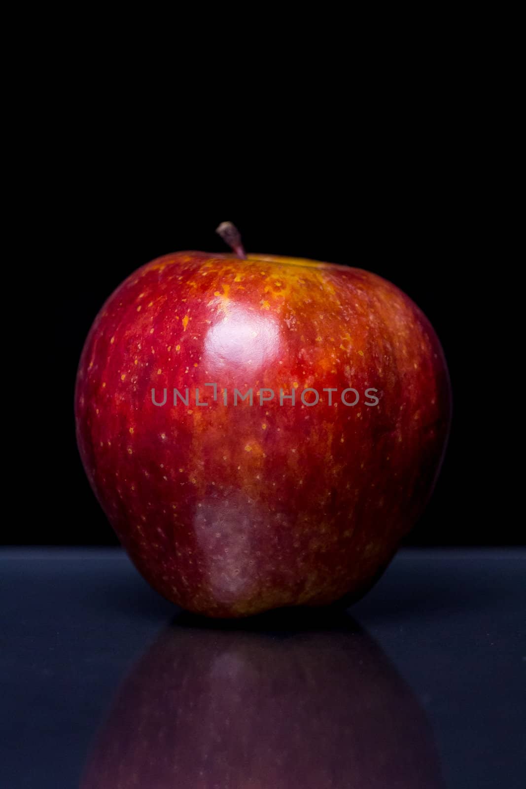 a Red Apple on a reflective black surface with black background
