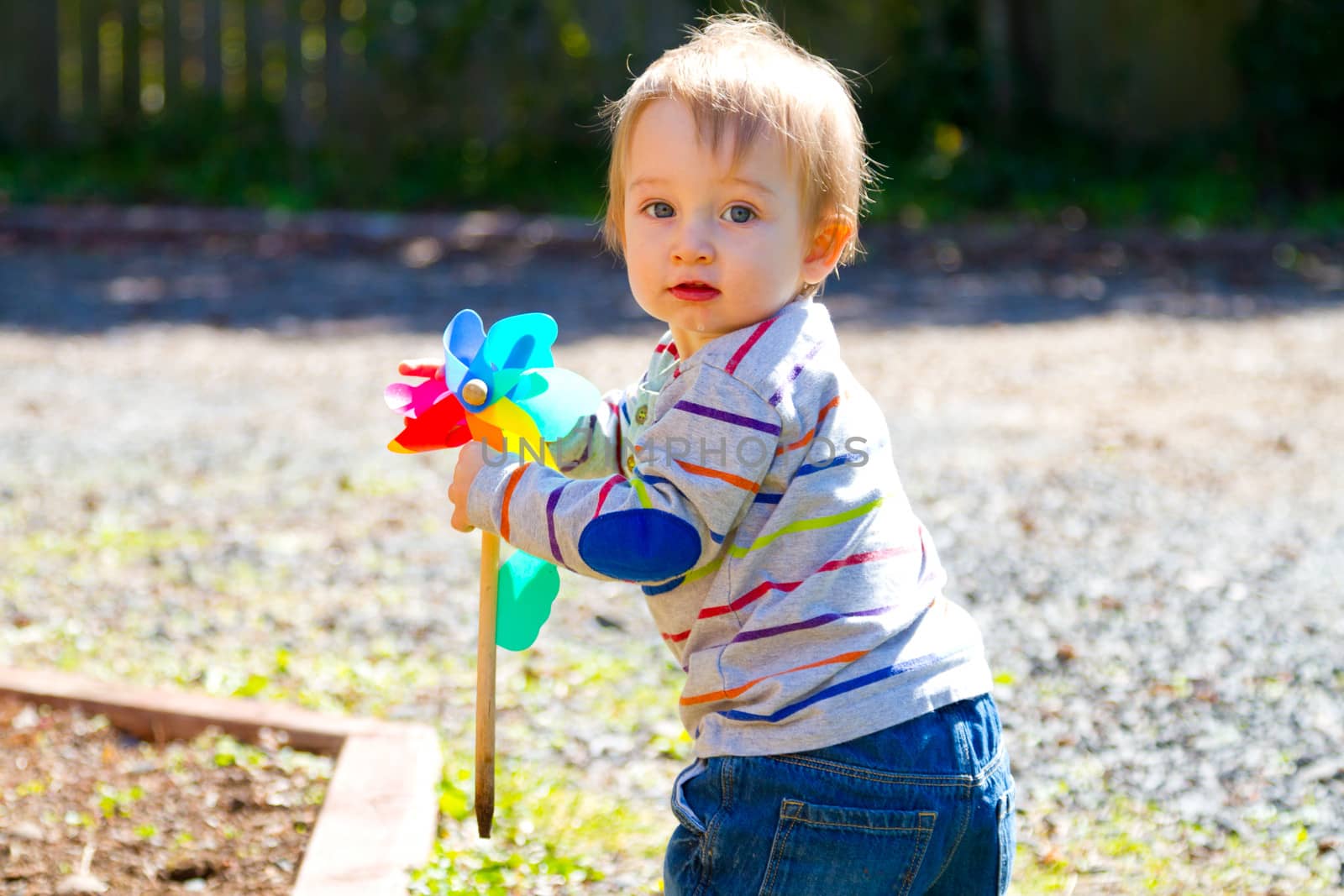 A one year old boy plays with a whirligig propeller pinwheel outside while wearing a striped shirt.