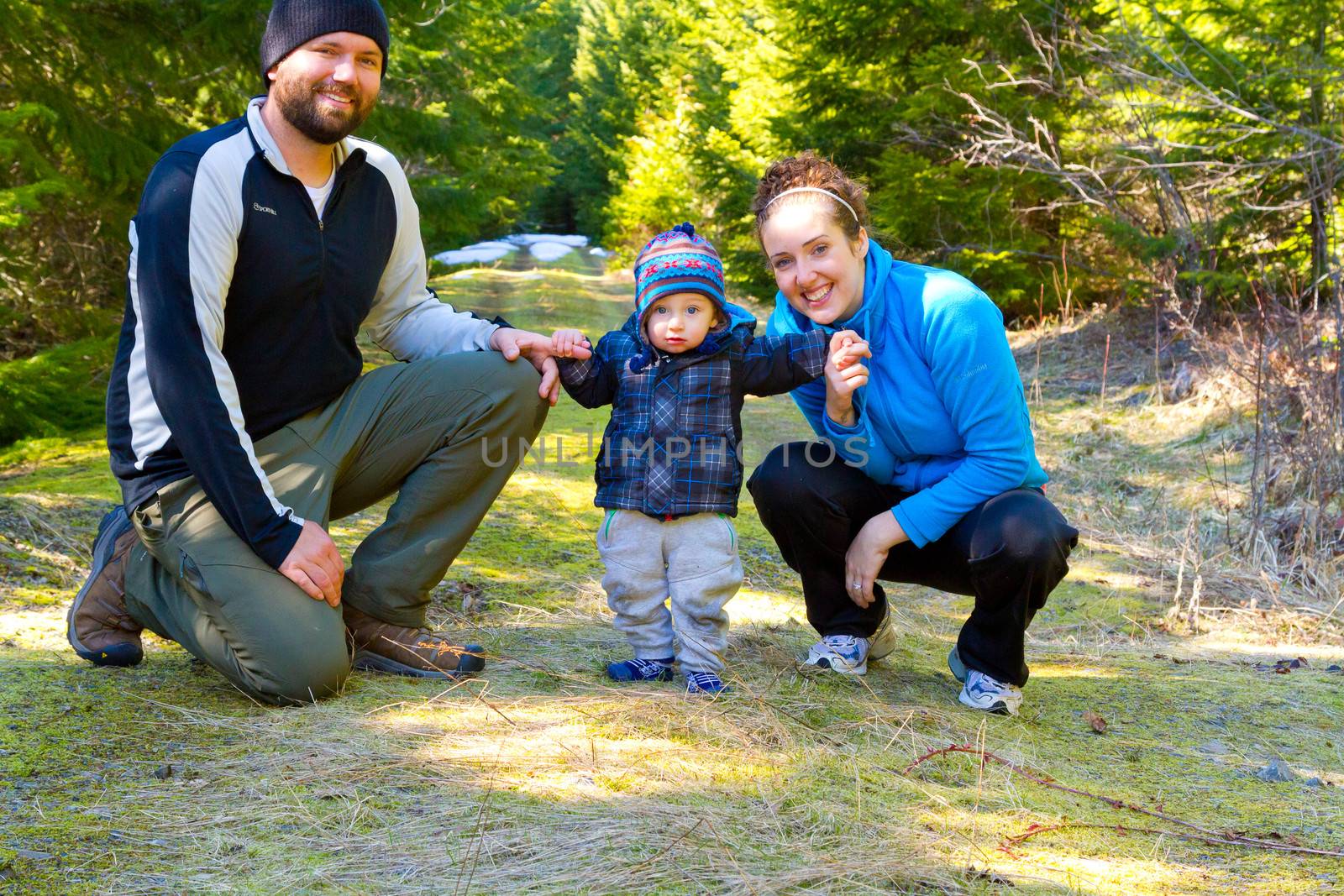 A family of three people stop for a moment to have some photos taken and pose for the camera while hiking in the Oregon wilderness during the spring time.