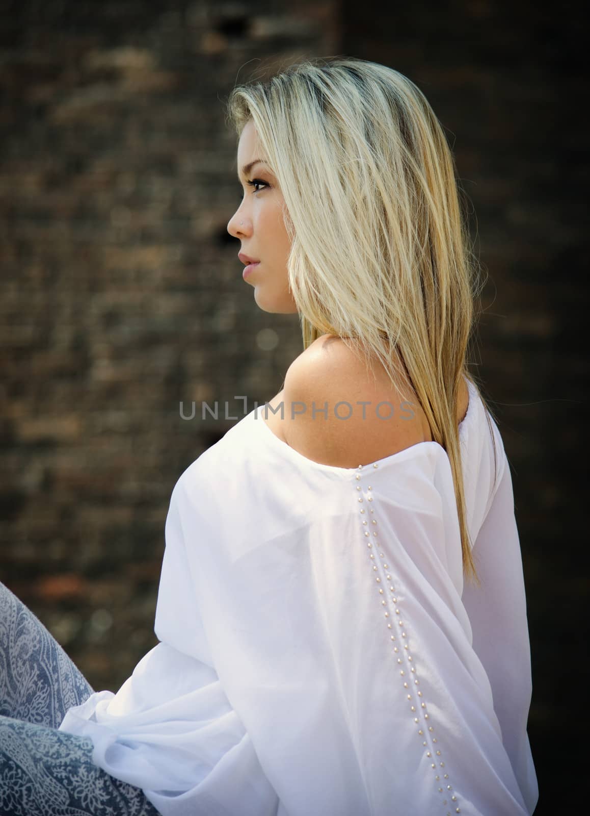 Profile of pretty blonde girl sitting outdoors with white shirt looking to a side