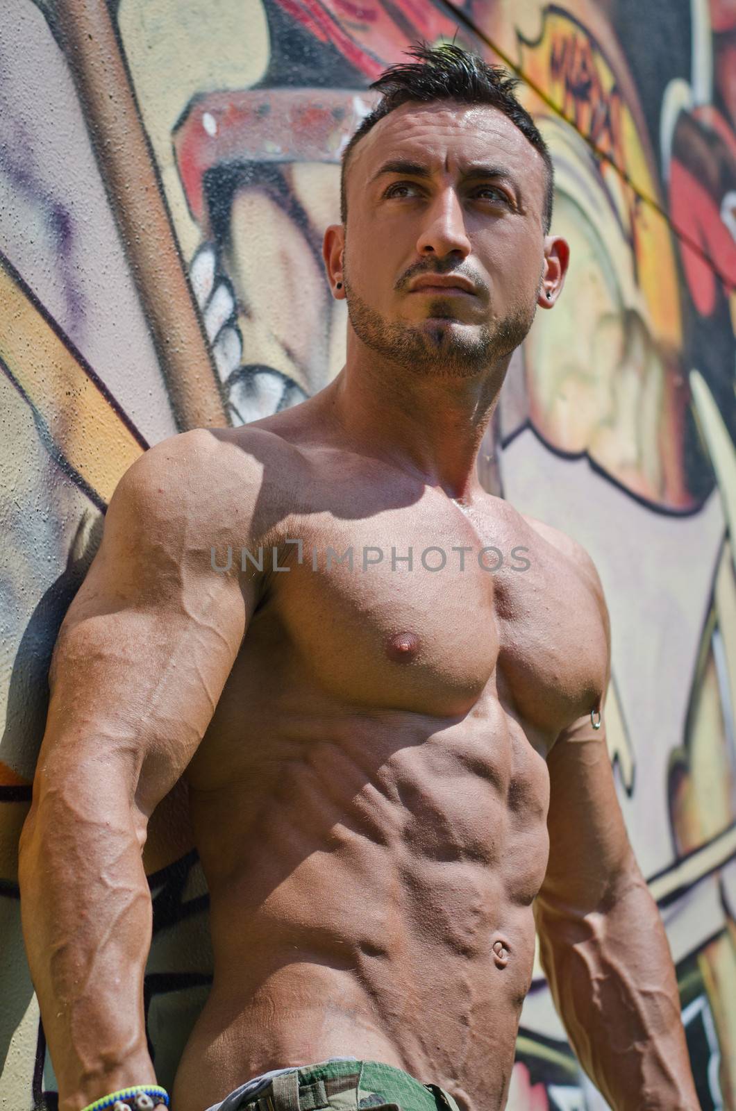 Attractive muscle man outdoors against graffiti wall looking to a side