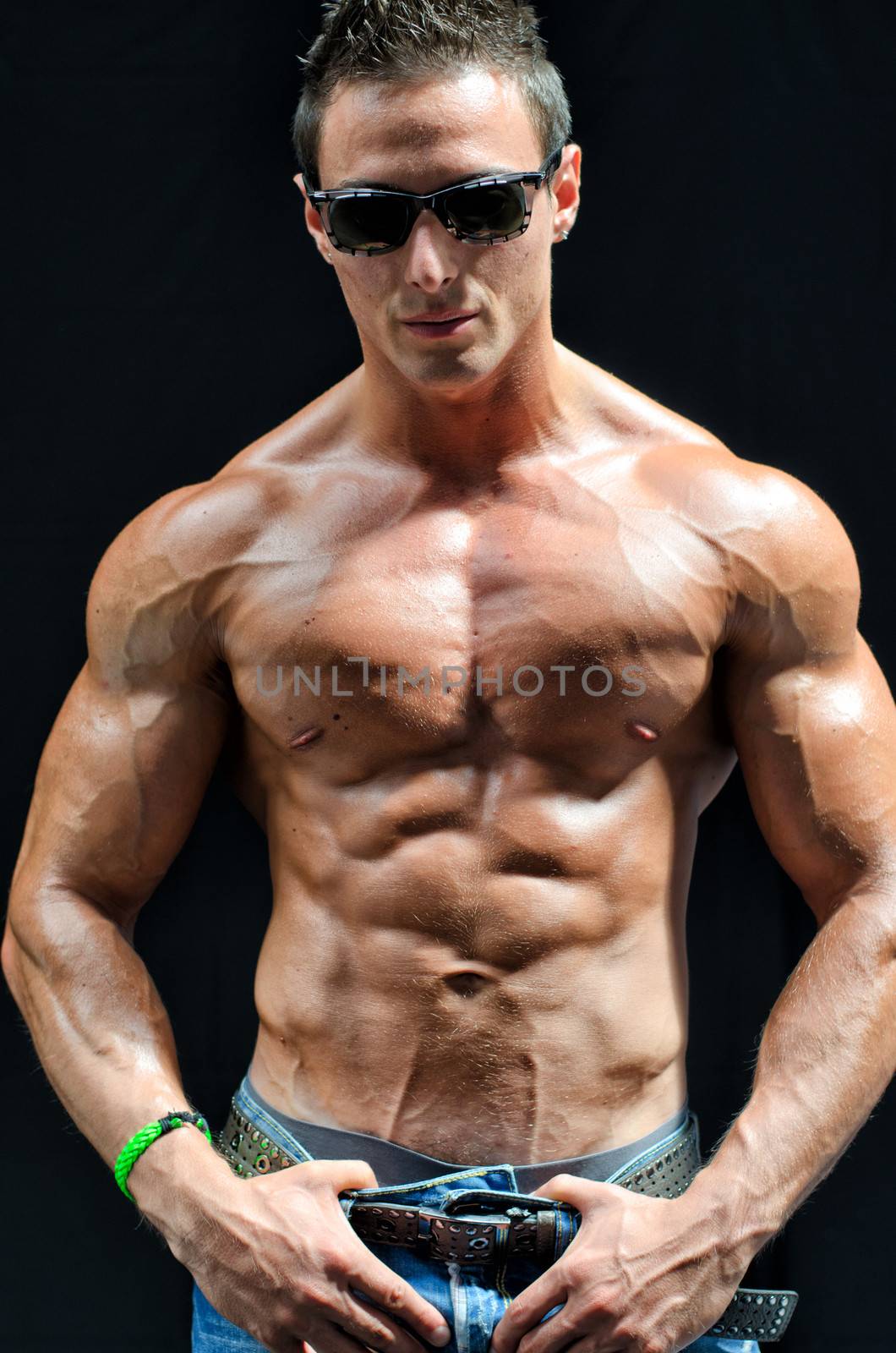 Handsome, muscular shirtless bodybuilder with jeans and sunglasses isolated on black
