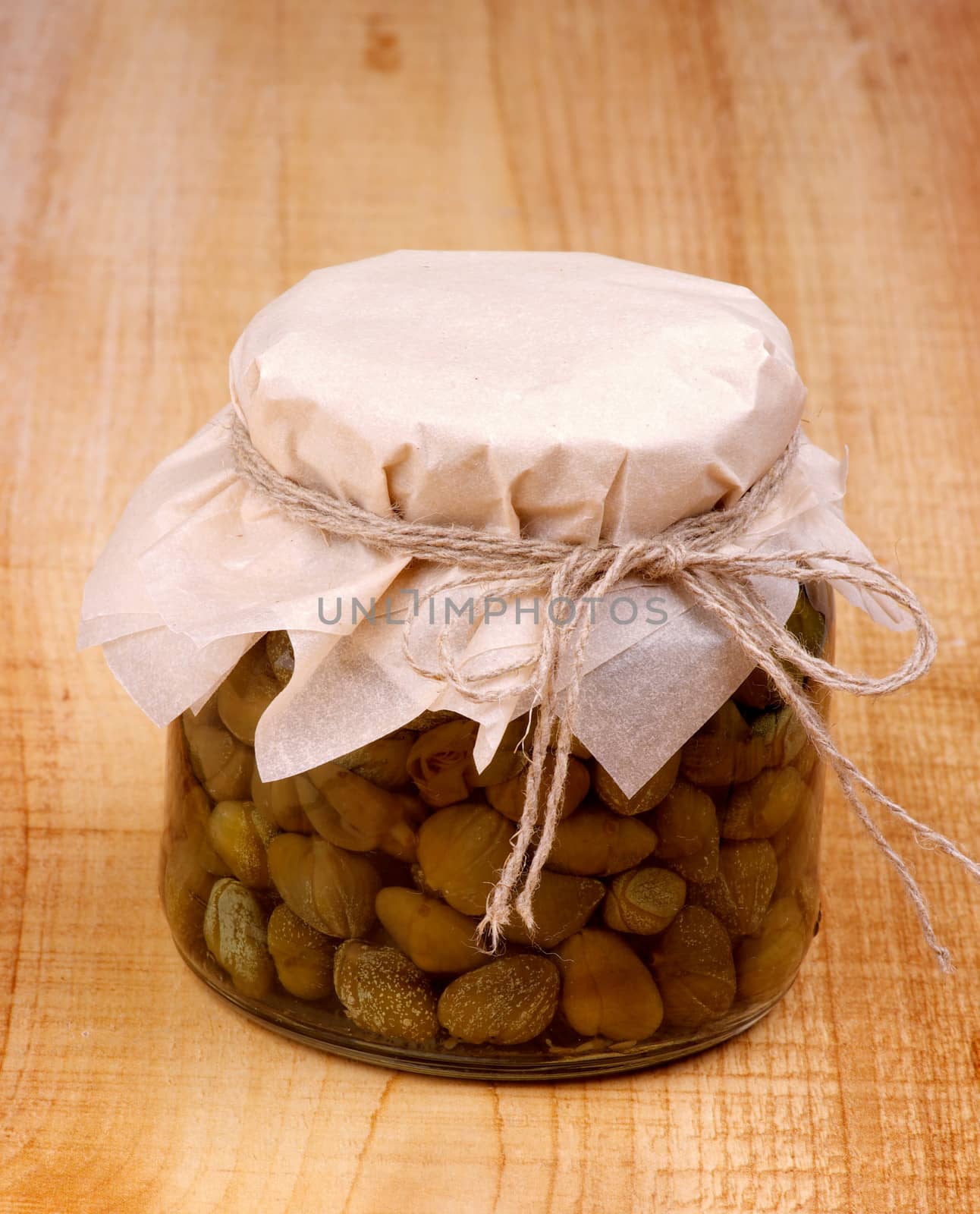 Glass Jar with Homemade Pickled Capers on Wooden background
