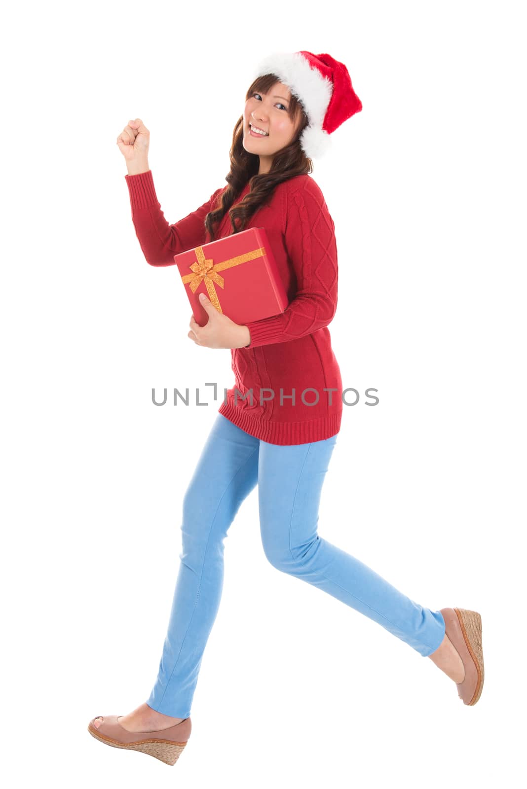Christmas woman running and holding gift wearing Santa hat. Standing in full body isolated on white background. Smiling woman portrait of a beautiful Asian model.