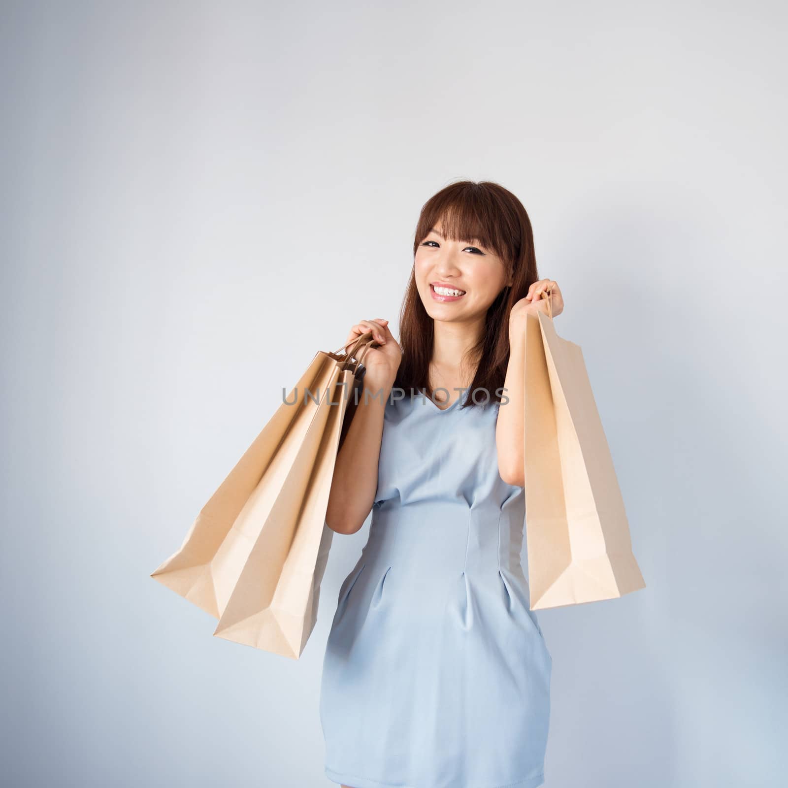 Shopping woman holding shopping bags looking at camera on blue background. Beautiful young Asian shopper smiling happy.