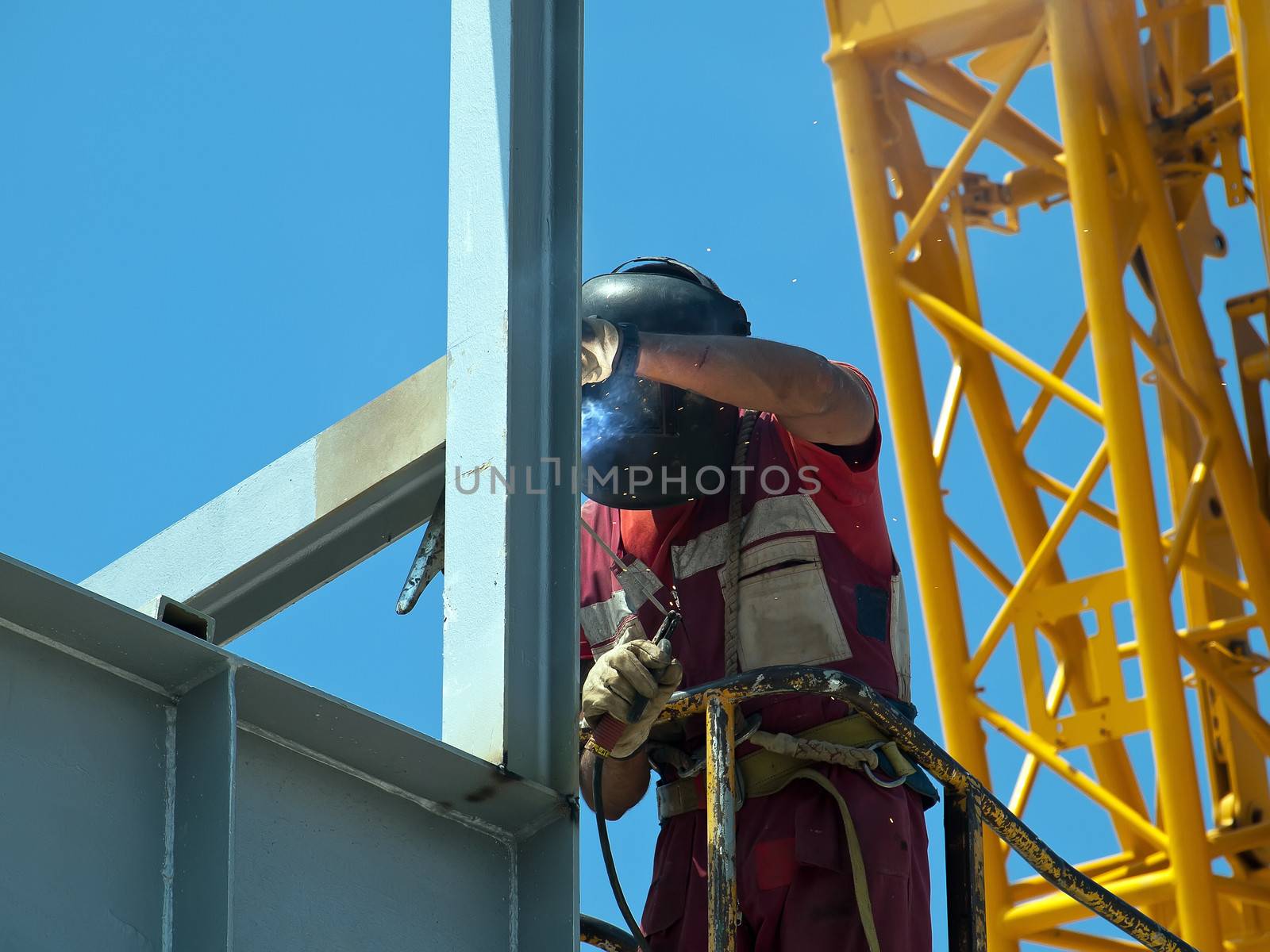 welder with protective mask welding metal construction, yellow crane on his back