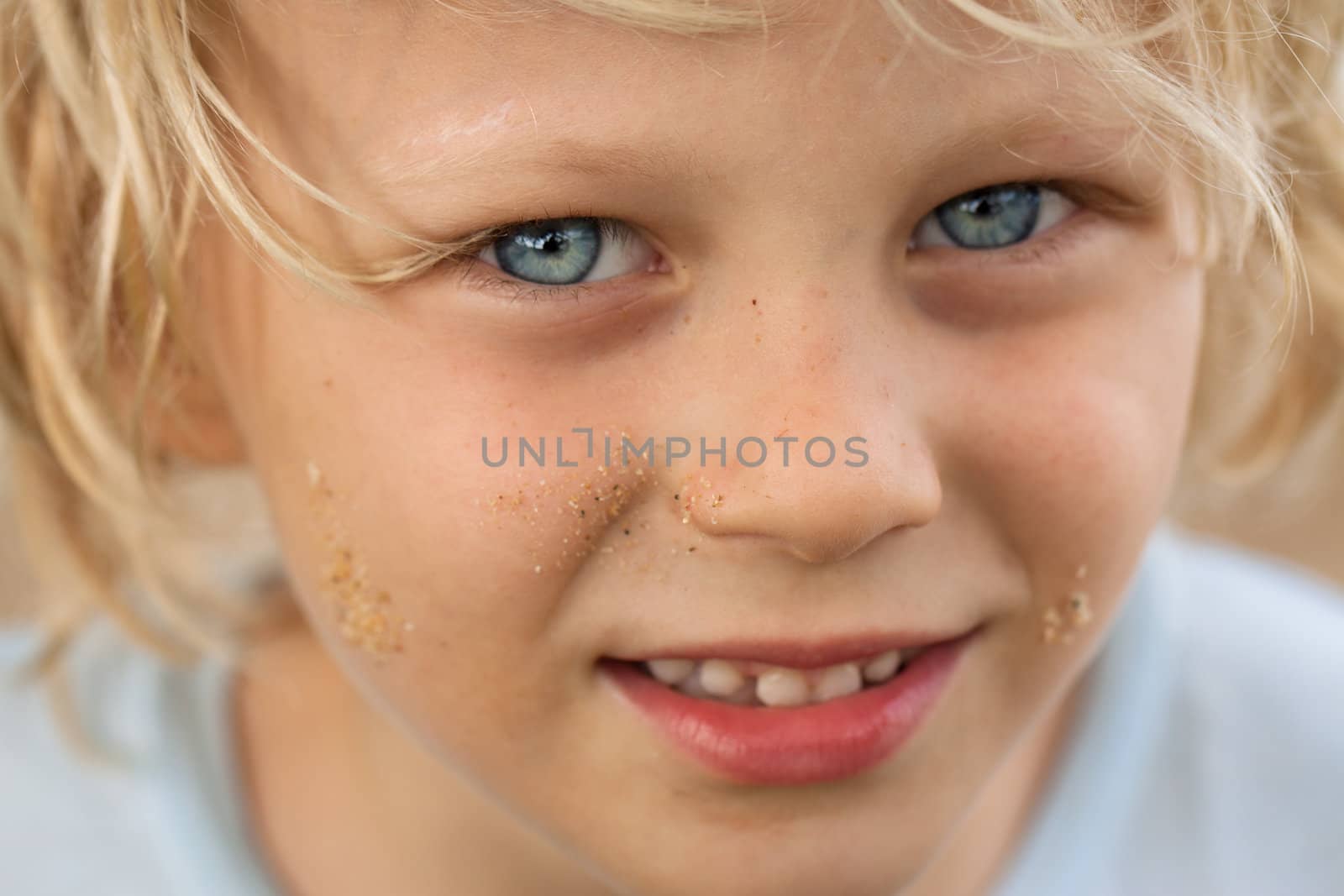 A close-up portrait of a cute happy boy who's been p[laying in the sand.